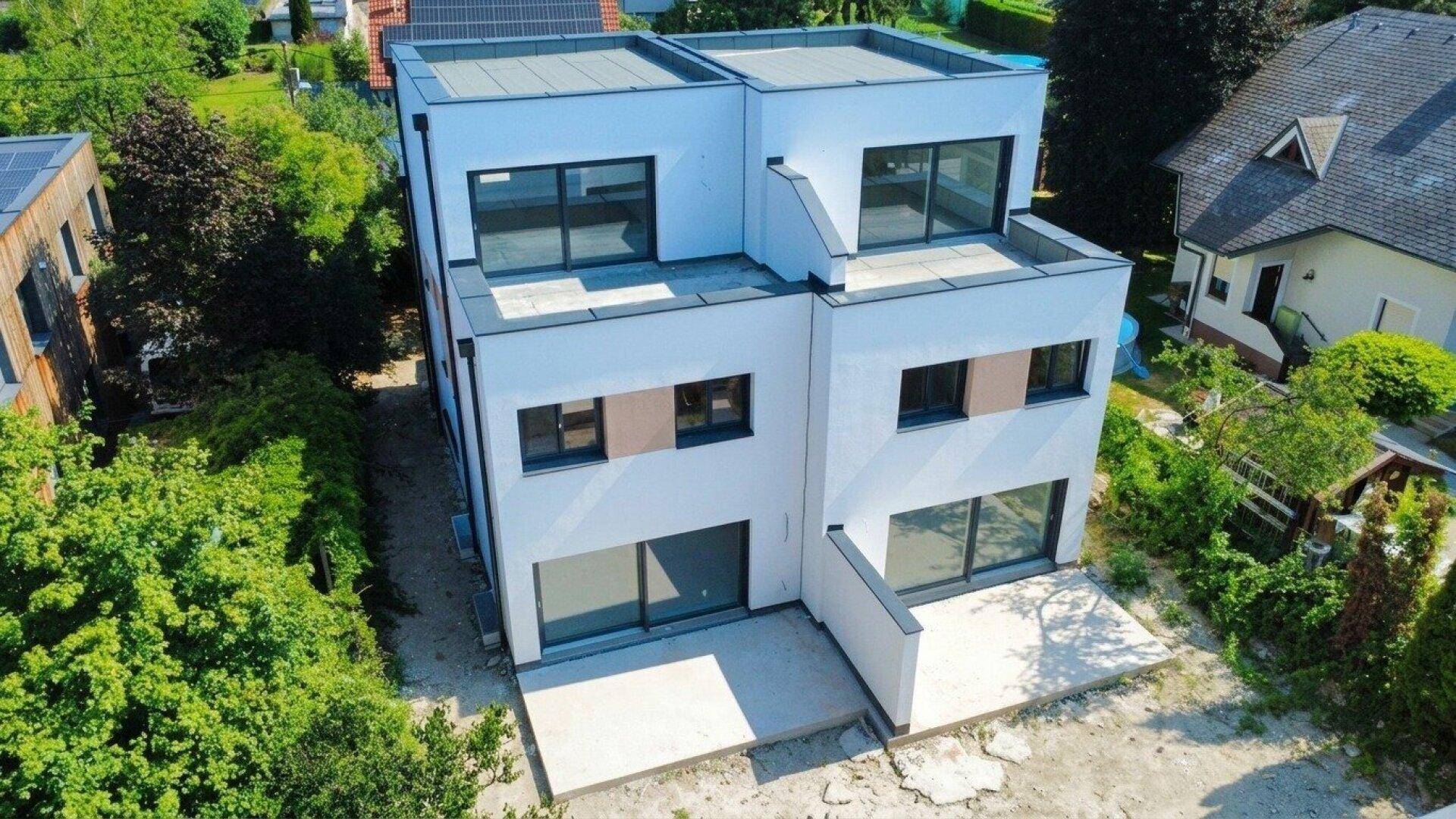 Ansicht eines modernen Doppelhauses mit weißer Fassade und großen Fensterfronten, umgeben von Natur.
