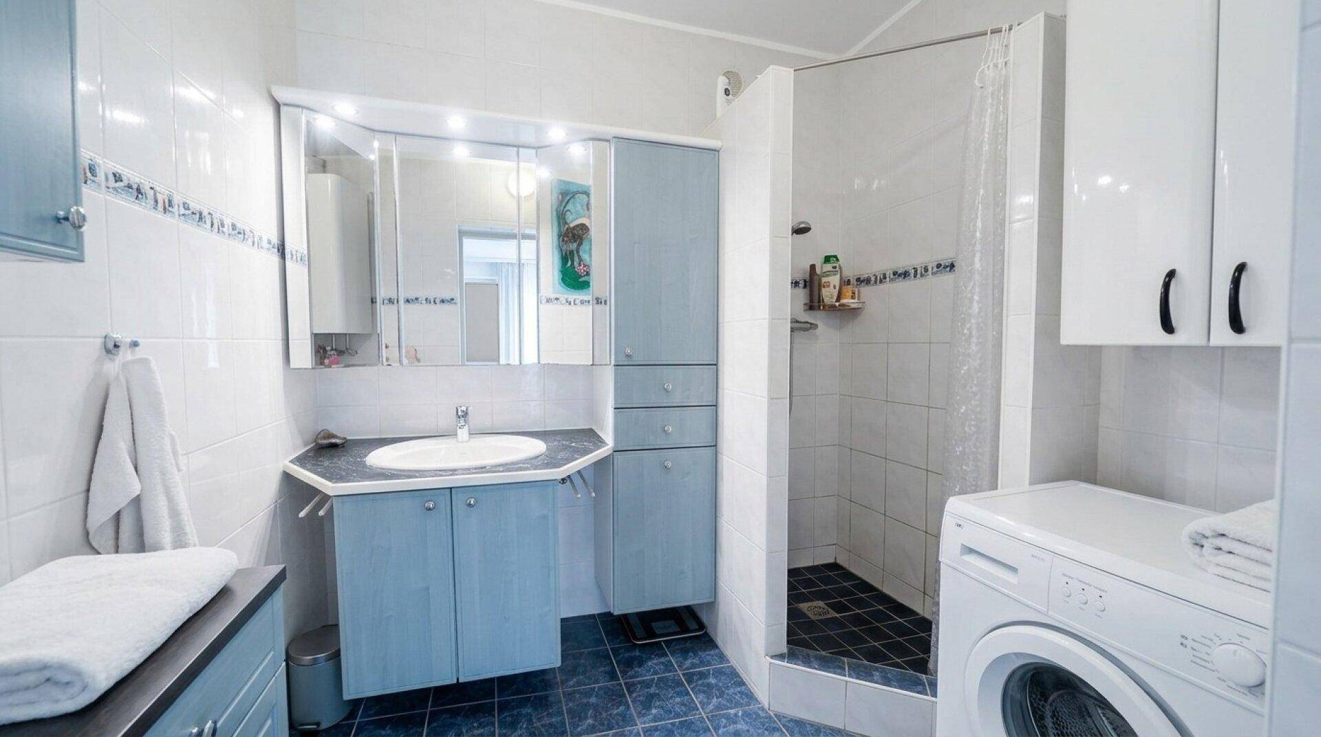 Badezimmer mit blauen Fliesen, Dusche, Waschbecken und integrierter Waschmaschine.