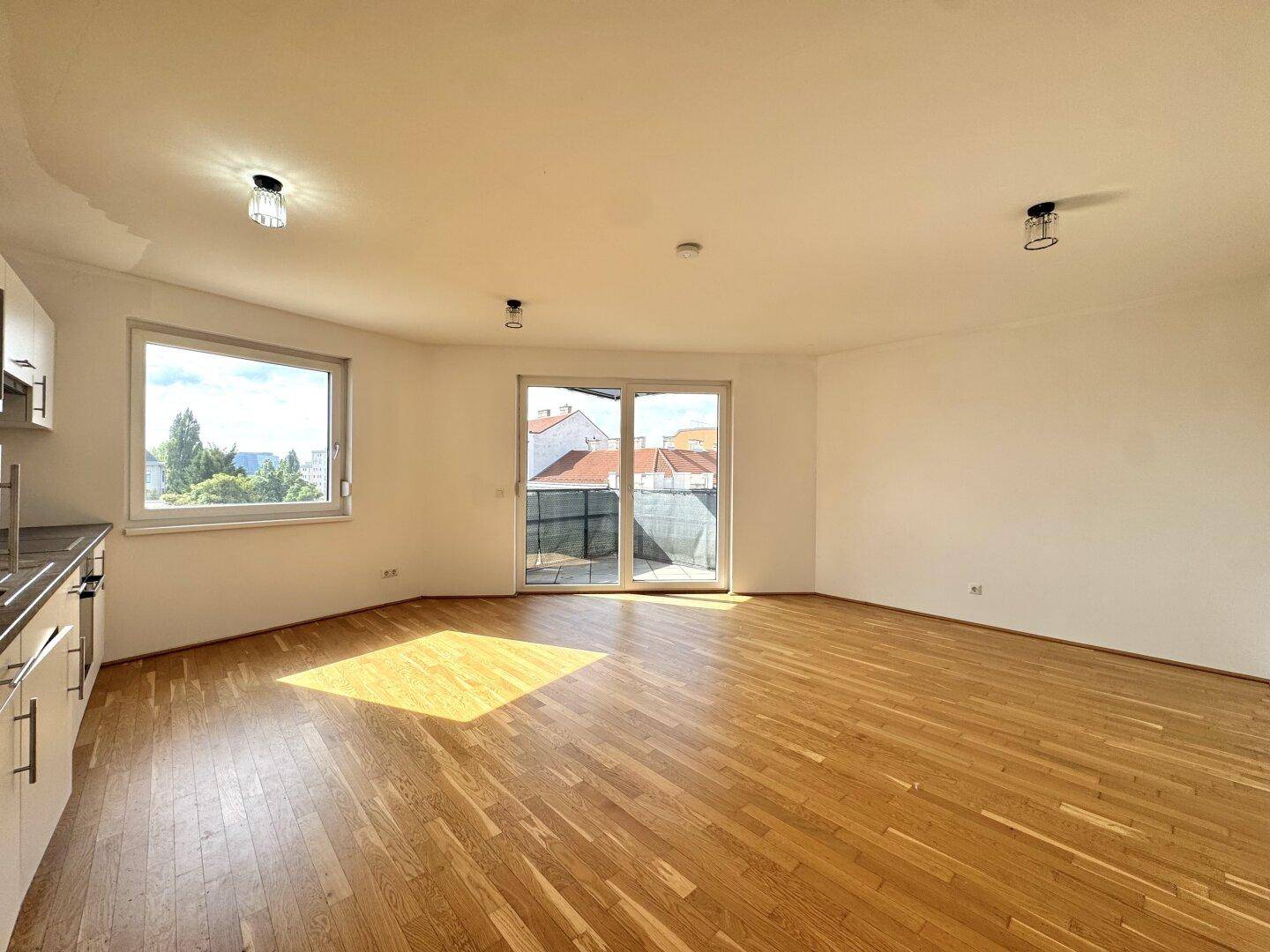 Geräumiger Wohnbereich mit Holzboden, großen Fenstern und viel Tageslicht.