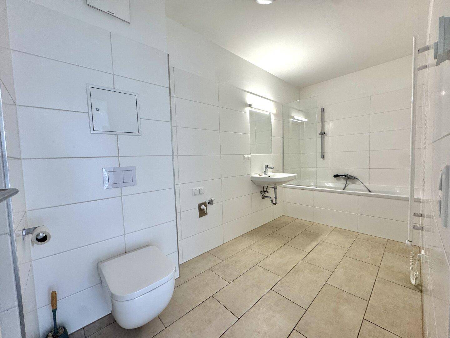 Modernes Badezimmer mit Badewanne, WC und weißen Fliesen an Wänden und Boden.
