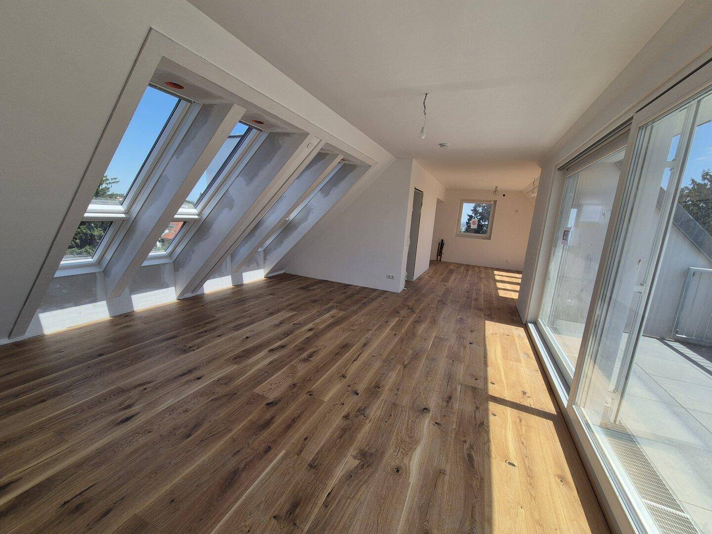 Geräumiges Wohnzimmer im Dachgeschoss mit Holzboden, Dachfenstern und Zugang zu einer Terrasse.