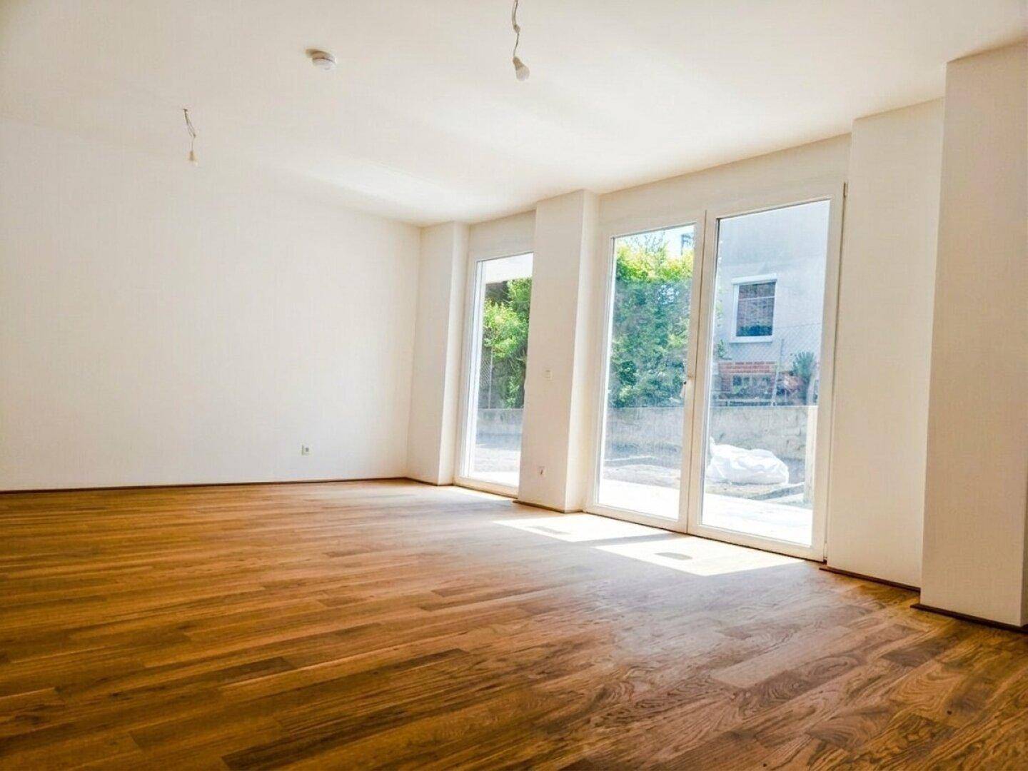 Heller, leerer Wohnraum mit großen Fenstern und hochwertigem Holzparkettboden.