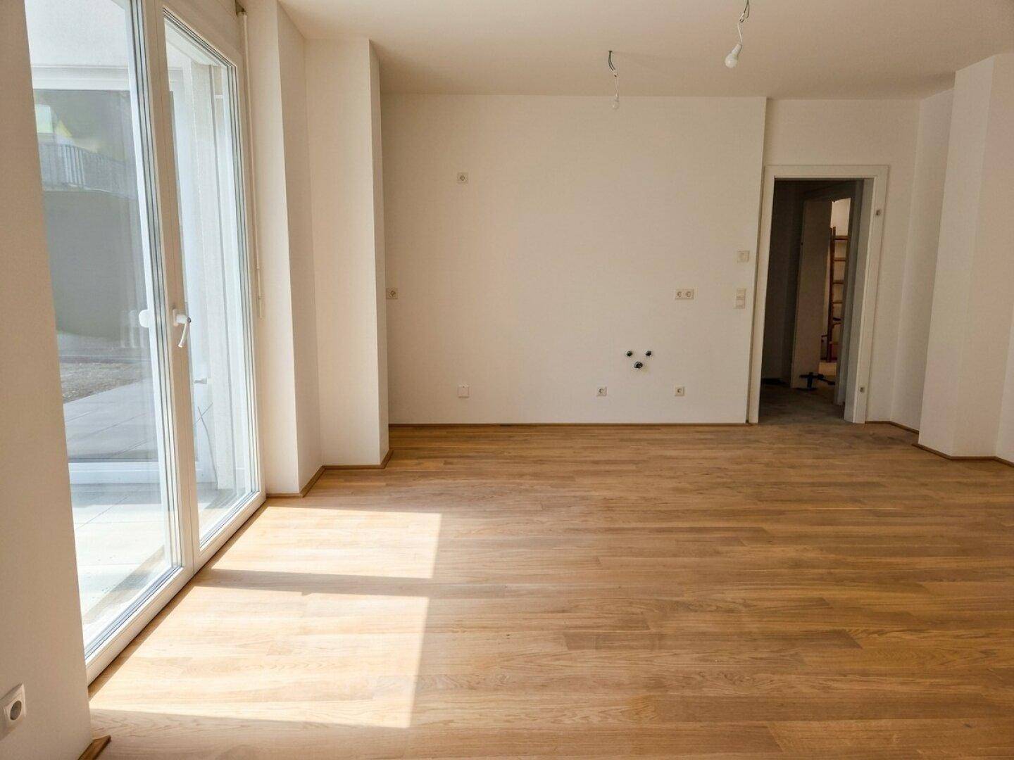 Geräumiger Wohnbereich mit Holzboden und Zugang zur Außenterrasse durch große Glastüren.