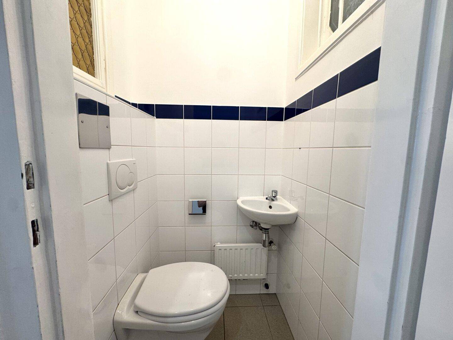 Kleines Gäste-WC mit Toilette, Eckwaschbecken und weiß-blauen Fliesen.