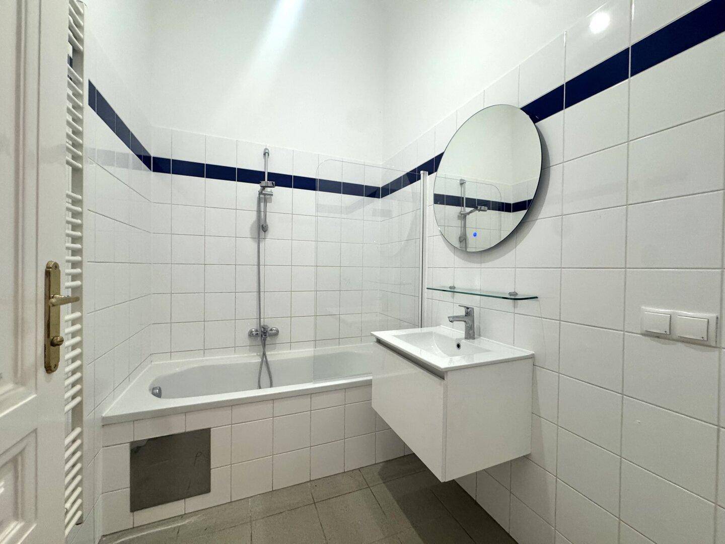 Modernes Badezimmer mit Badewanne, Duschfunktion, stilvollem Waschtisch und runden Spiegel.