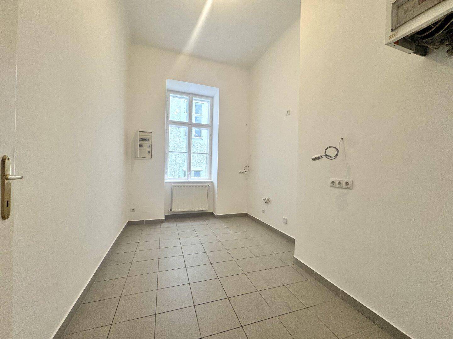 Funktionaler Raum mit Fliesenboden und Fenster, ideal als Abstellraum oder zukünftige Küche.