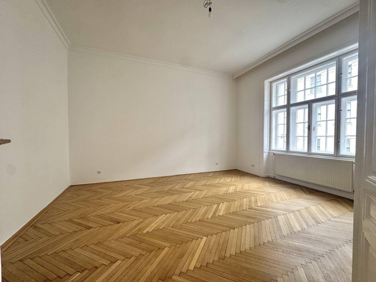 Ruhiges Schlafzimmer mit elegantem Fischgrätparkett und einem großen Fenster für natürliche Belichtung.