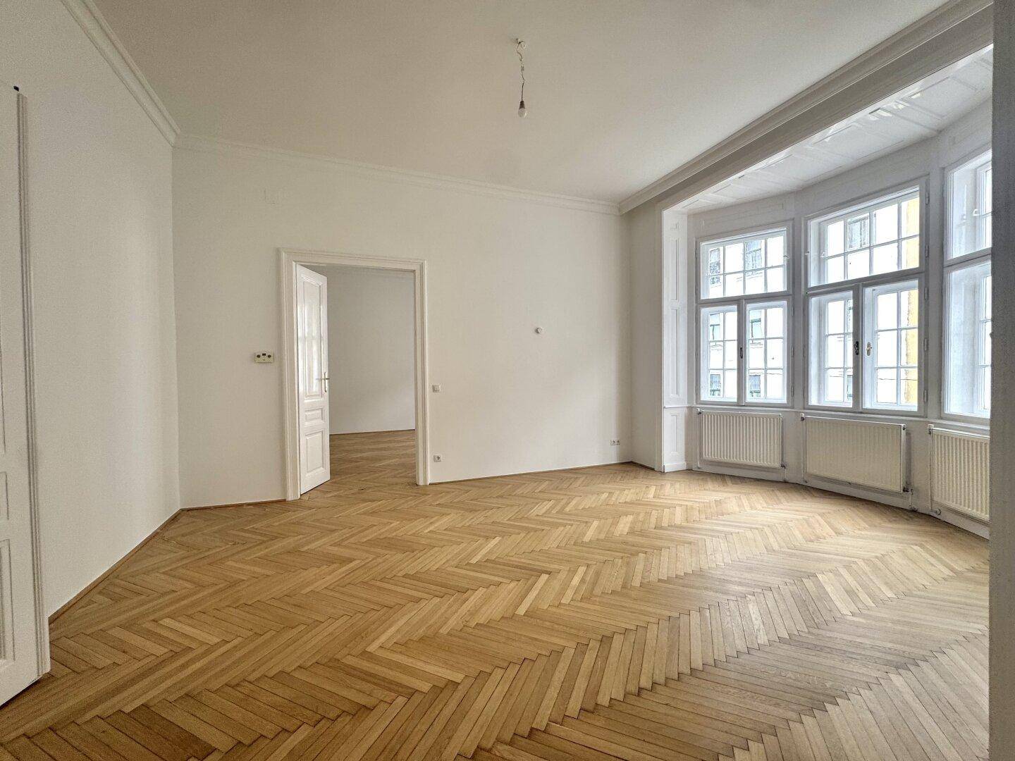 Helles Wohnzimmer mit klassischem Fischgrätparkett und einem großen Erker, der den Raum erweitert.