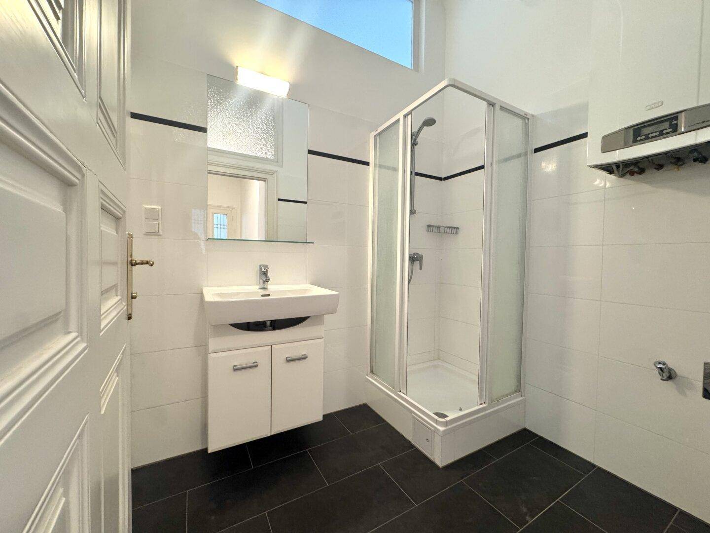 Modern gefliestes Badezimmer mit Duschkabine, Waschbecken und Gastherme.