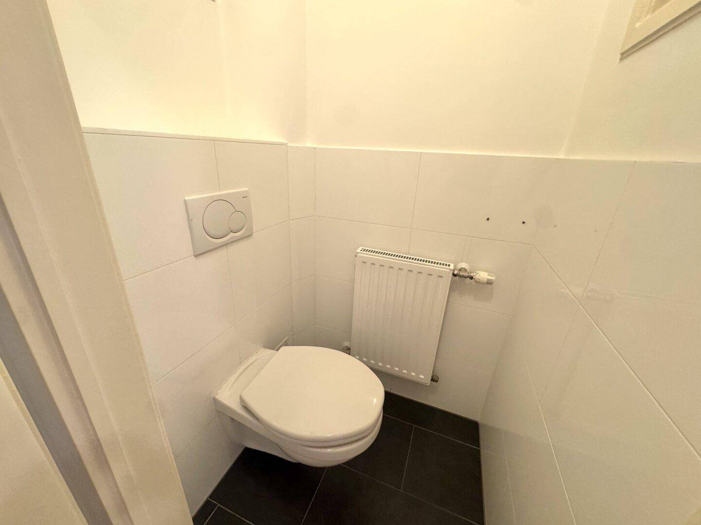 Separates WC mit Wand-WC und Heizkörper, weiß gefliest.