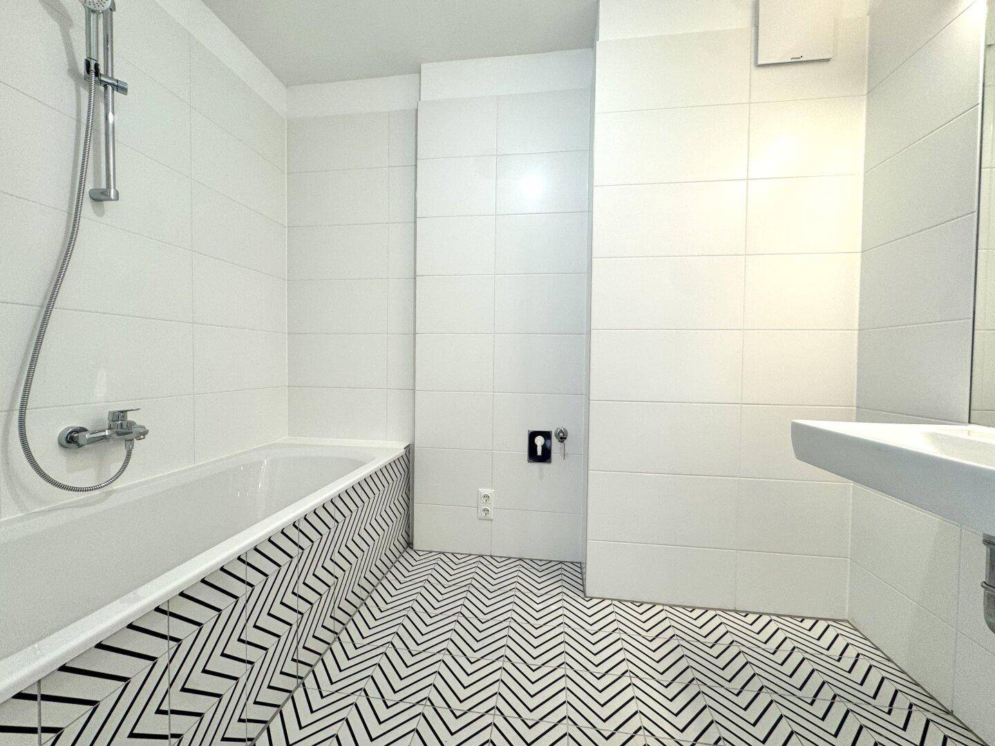 Modernes Badezimmer mit weiß gefliesten Wänden, Badewanne und auffälligem schwarz-weißem Fliesenboden.