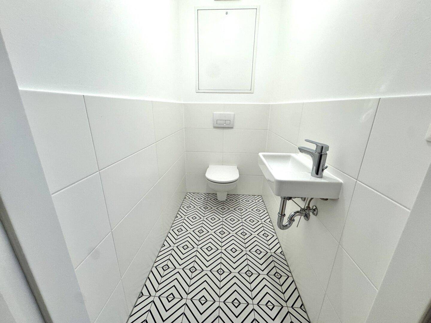 Kleines Gäste-WC mit modernen Fliesen, wandhängender Toilette und einem kompakten Waschbecken.