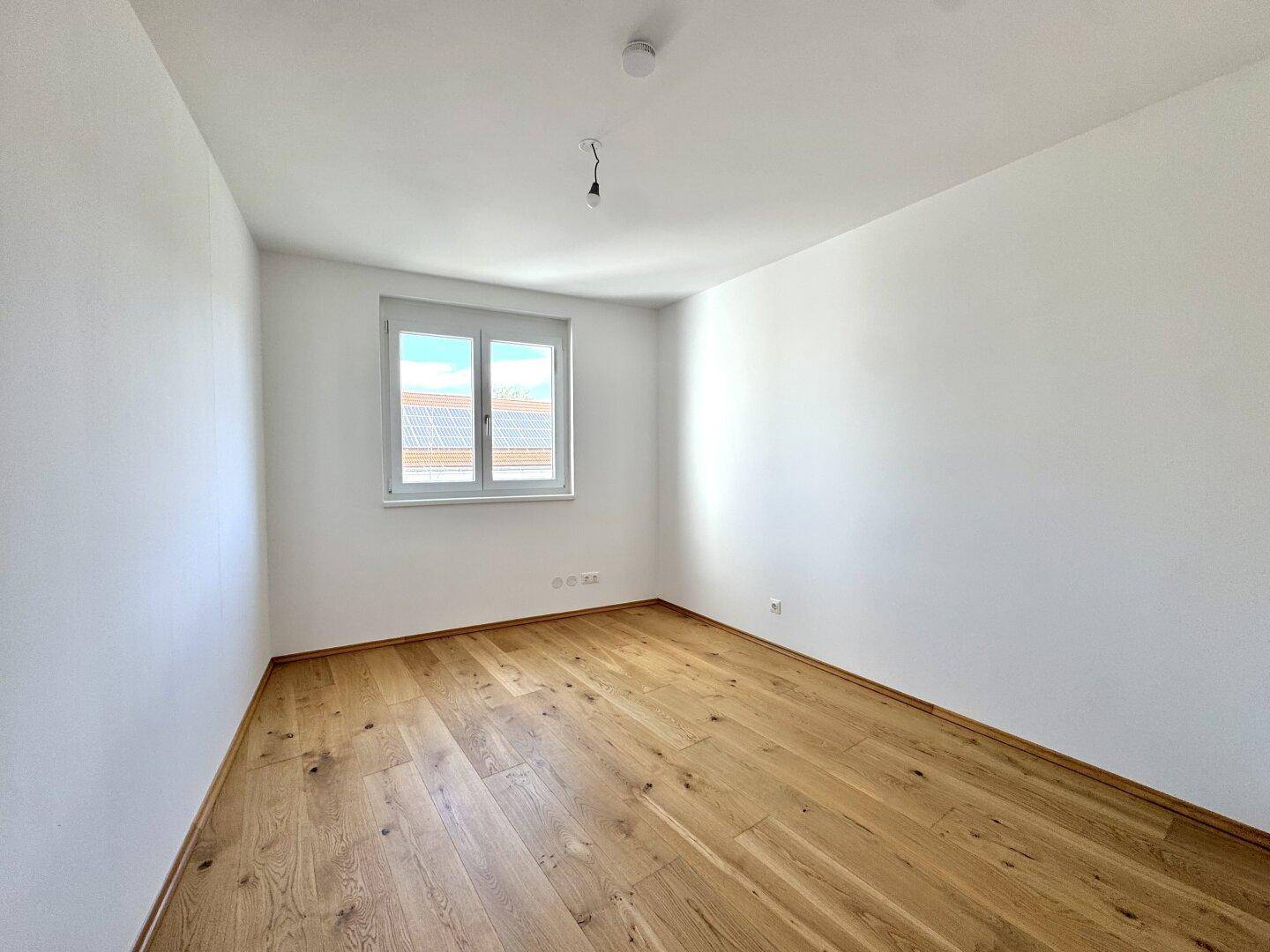 Helles Zimmer mit Holzboden und einem großen Fenster, ideal als Schlaf- oder Arbeitszimmer.