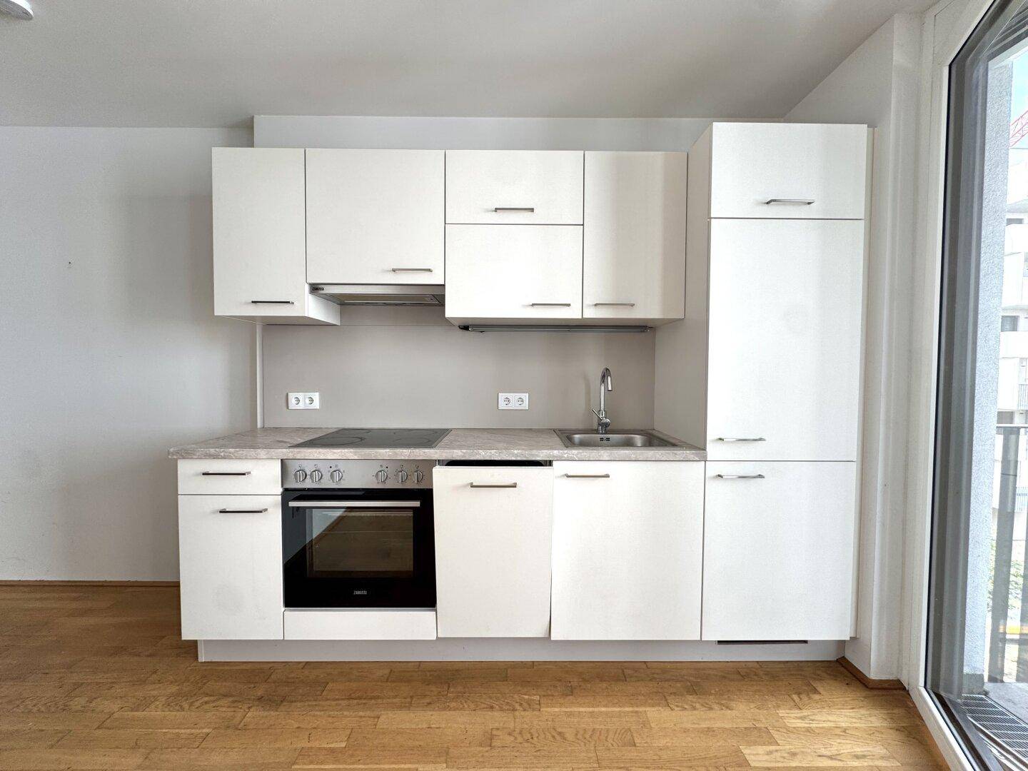 Moderne, kompakte Einbauküche in Weiß mit integrierten Geräten und Holzboden.