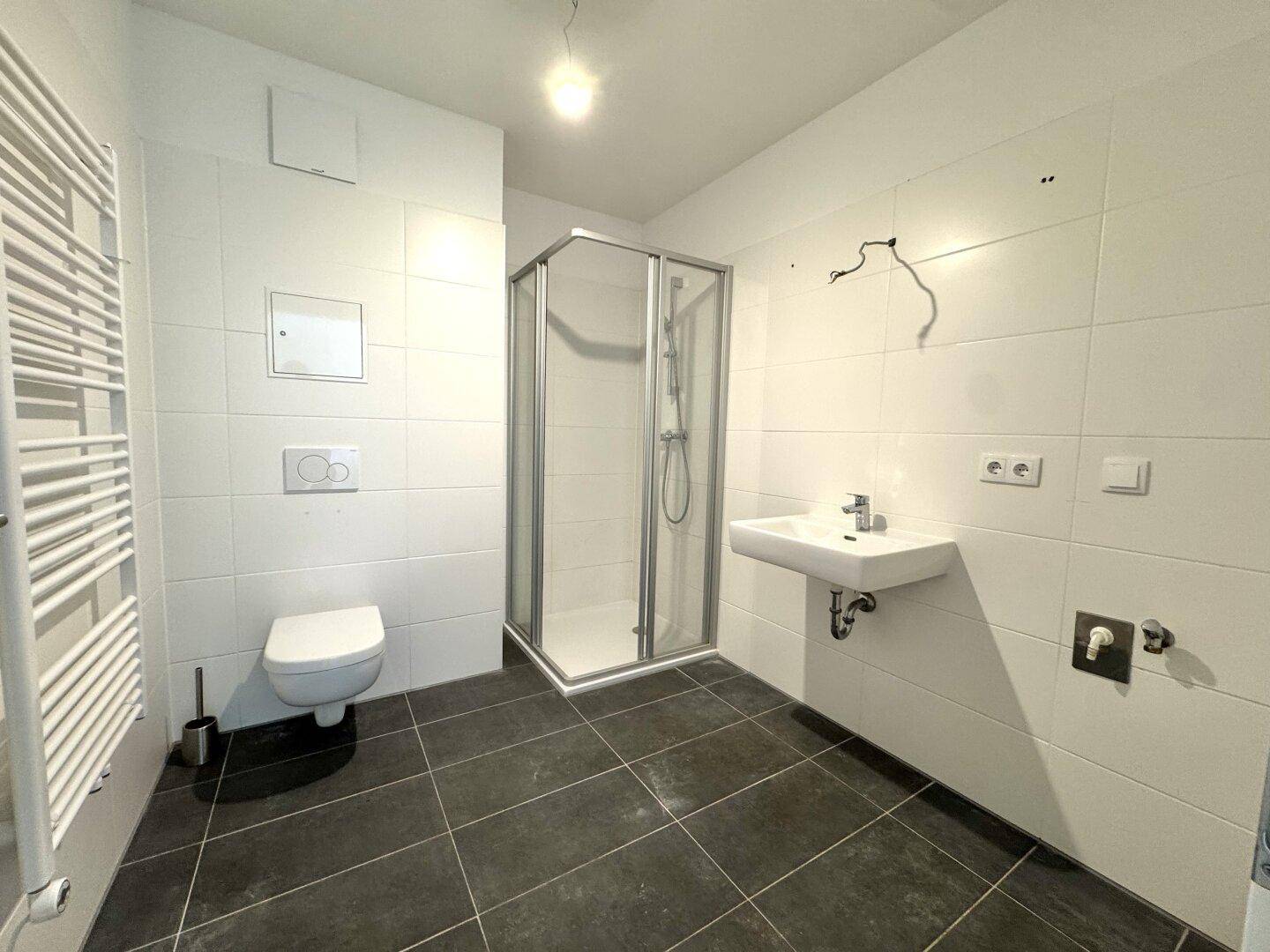 Modernes Badezimmer mit dunklen Fliesen, Duschkabine, WC und beheiztem Handtuchhalter.