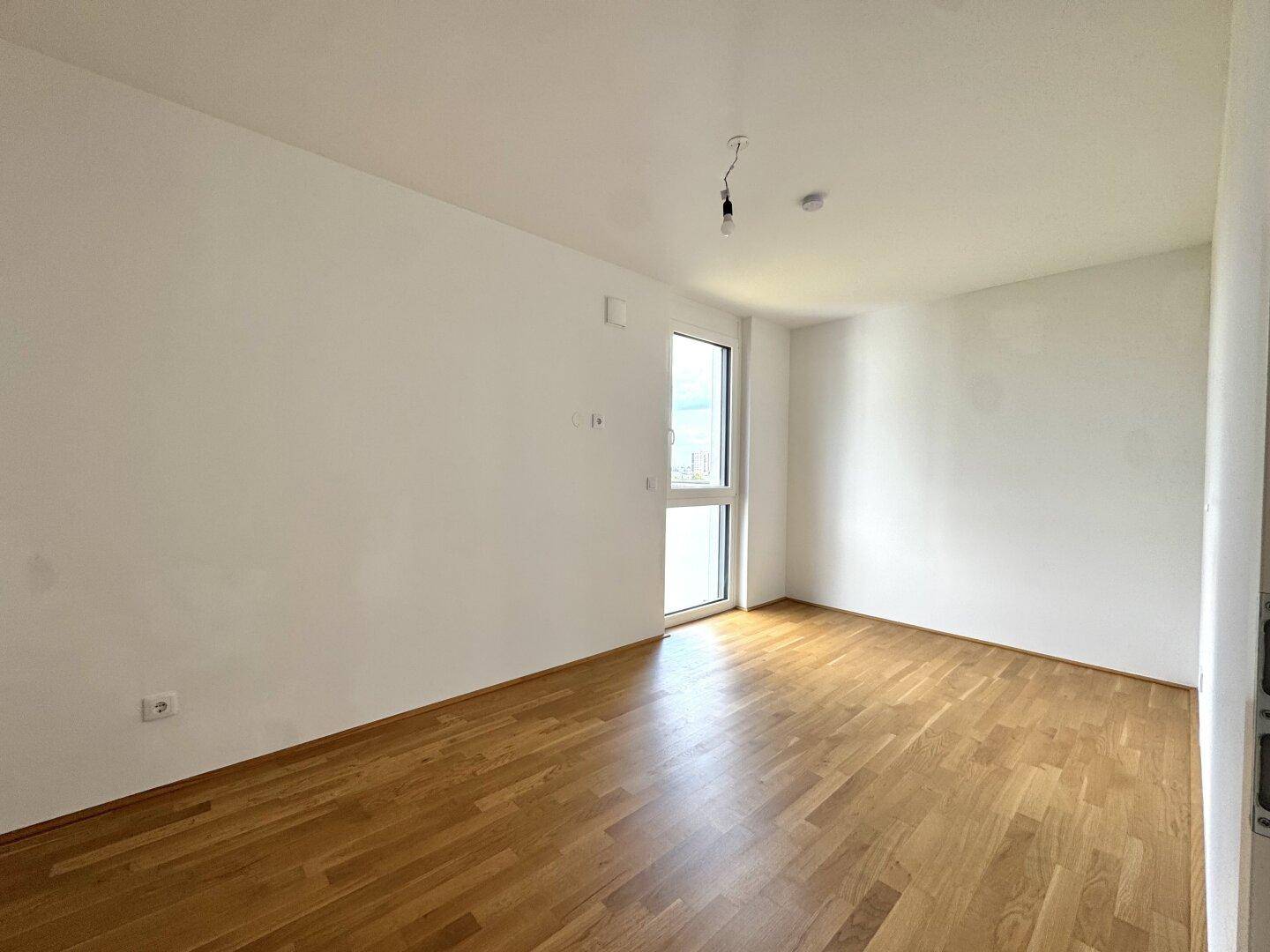 Leeres Schlafzimmer mit hellem Holzparkettboden und einem großen Fenster.