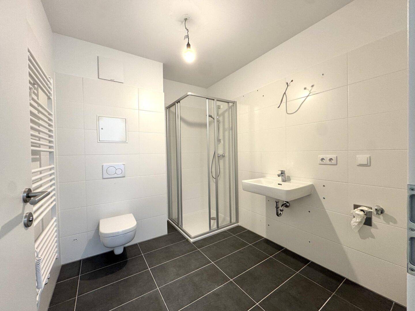 Modernes Badezimmer mit Duschkabine, Wand-WC, Waschbecken und Handtuchheizkörper.