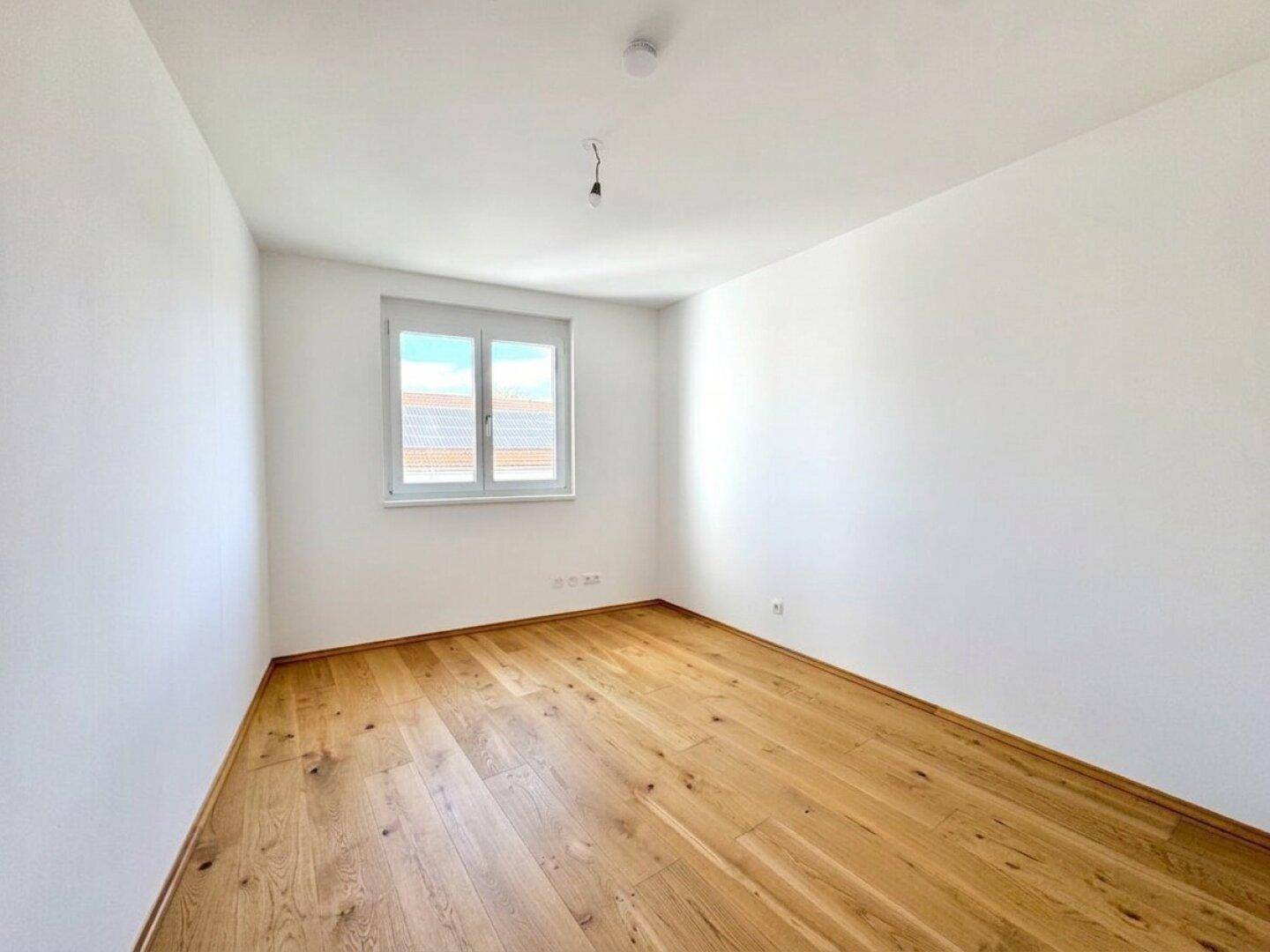 Leeres Schlafzimmer mit hellem Holzboden und einem Fenster für natürliches Licht.