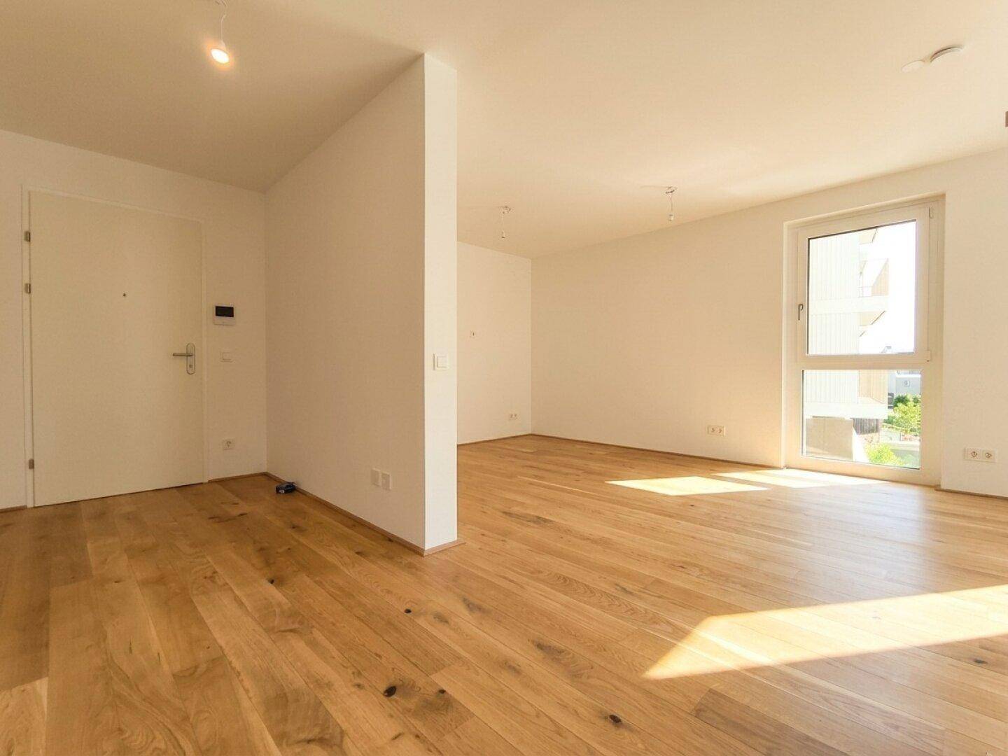 Geräumiger, heller Wohnbereich mit Eichenparkett und Zugang zur Wohnungstür.
