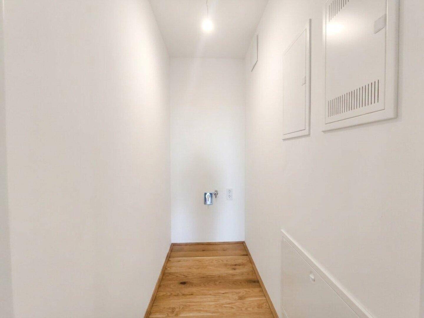 Schmaler Flur mit Holzfußboden und Wandpaneelen, möglicherweise ein Hauswirtschaftsraum.