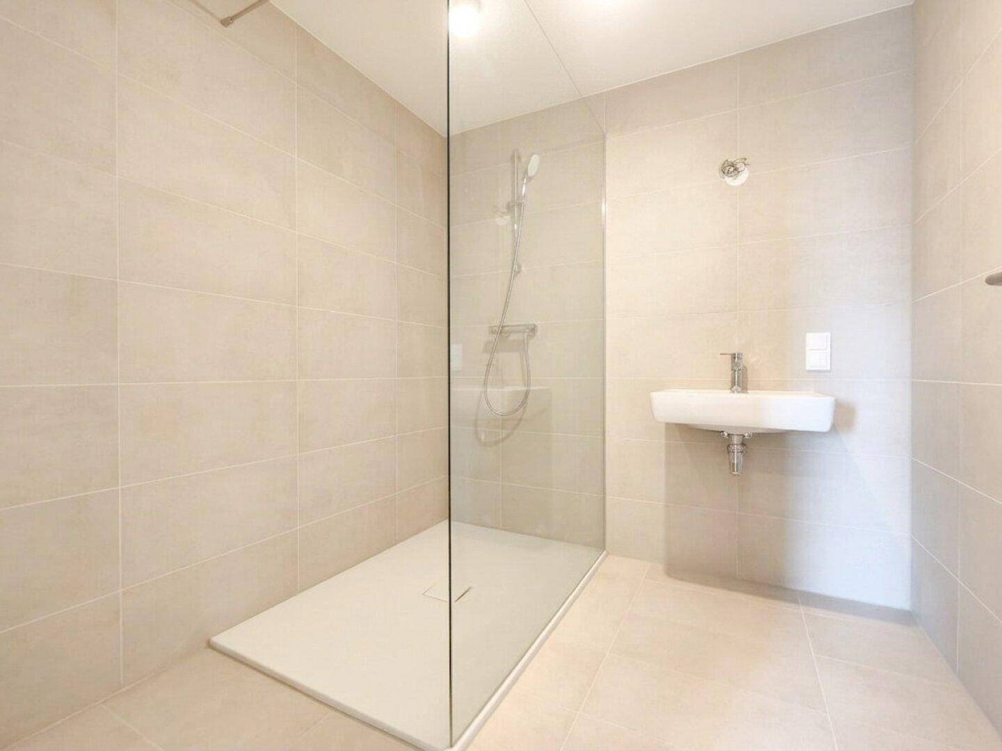 Modernes Badezimmer mit begehbarer Dusche, beigefarbenen Fliesen und minimalistischem Waschbecken.