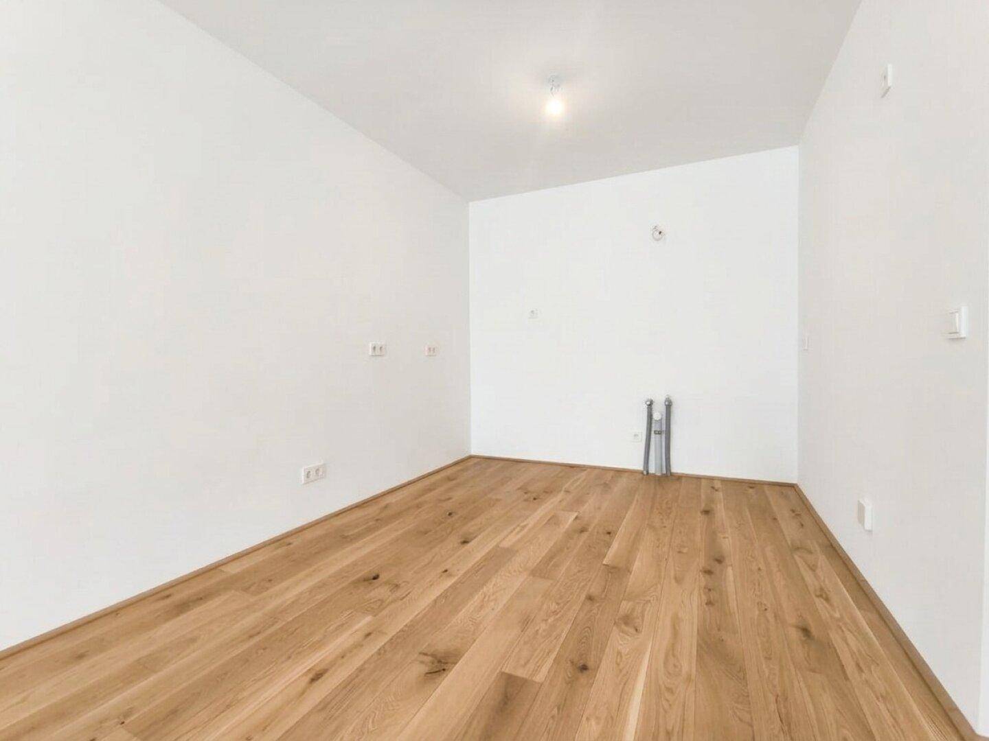 Leerer Küchenraum mit Anschlüssen für Spüle und Geräte sowie hellem Holzboden.