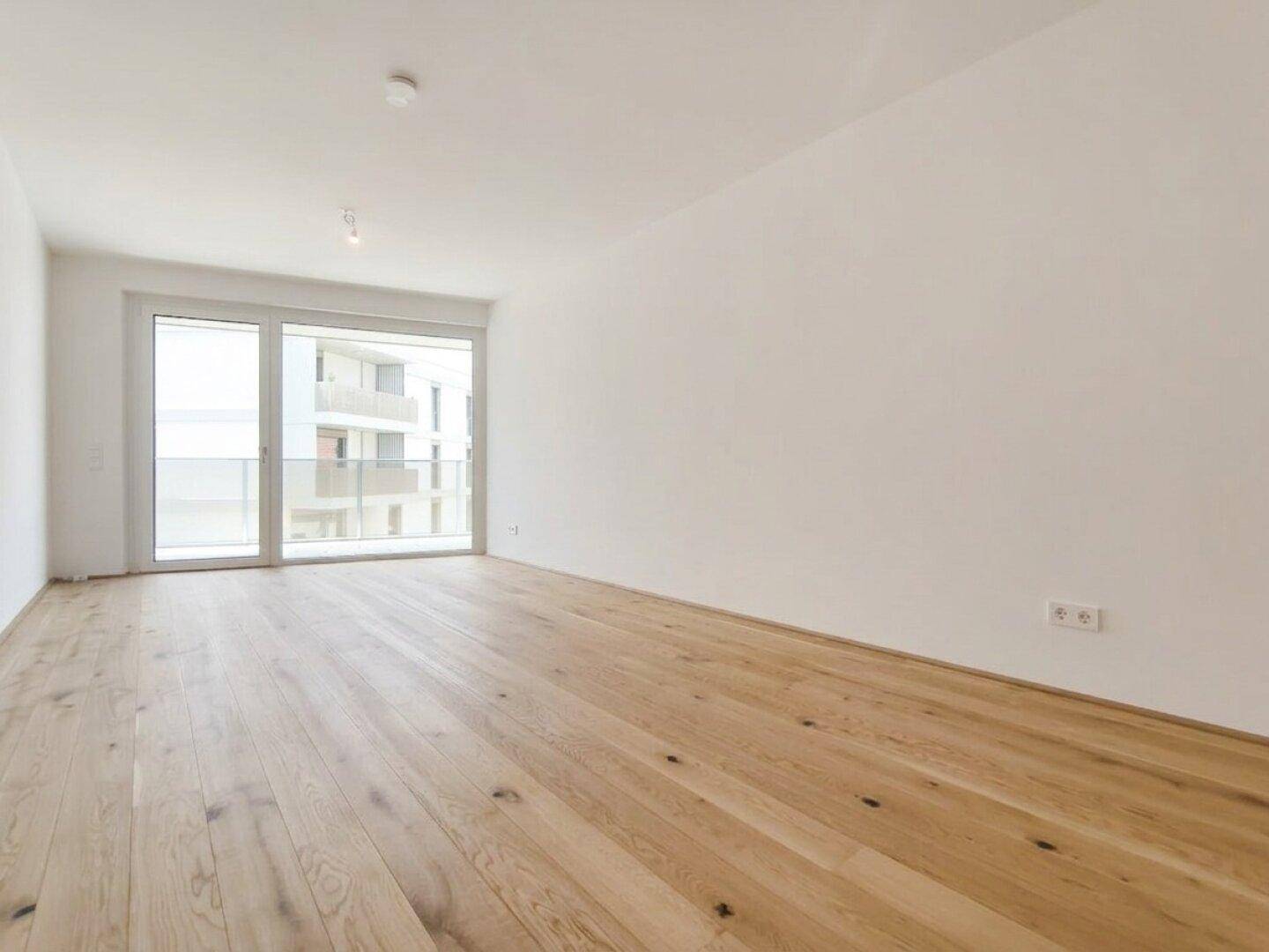 Helles Schlafzimmer mit Holzboden und großen Fenstern, die viel Tageslicht hereinlassen.