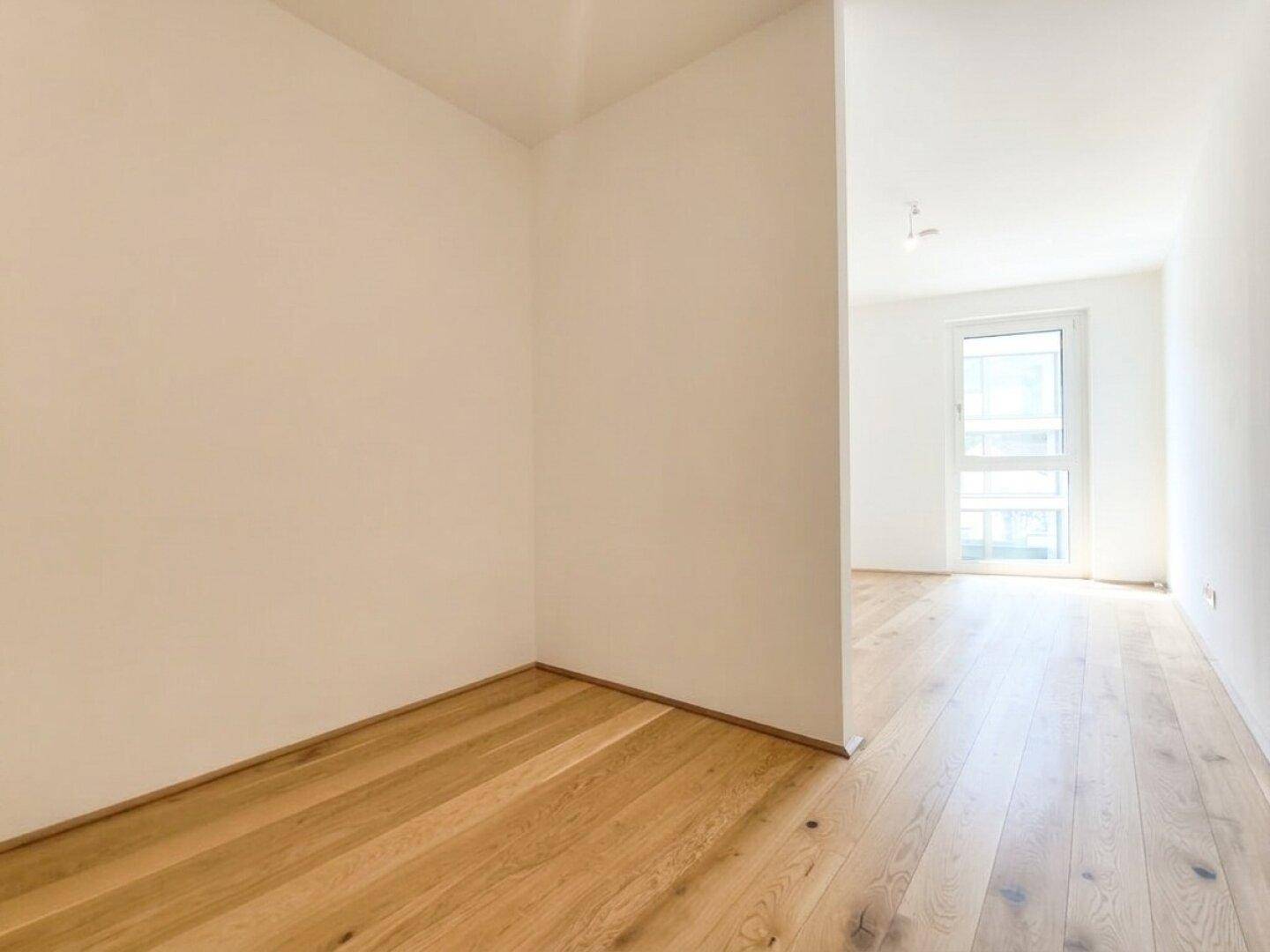 Heller Flur mit Holzboden und weiß gestrichenen Wänden, der zu weiteren Räumen führt.