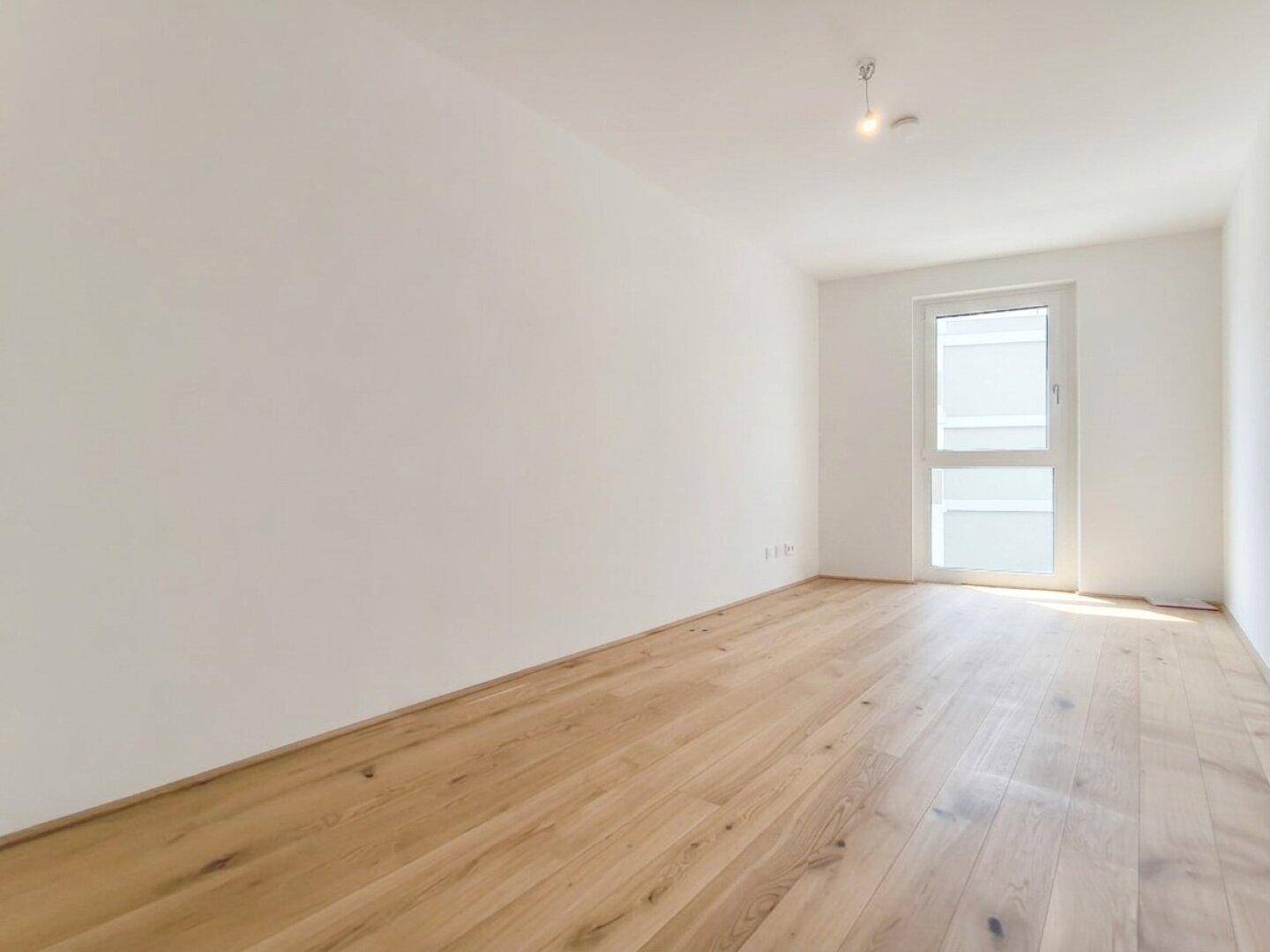 Helles Zimmer mit Holzboden und einem Fenster, das den Raum mit Tageslicht versorgt.