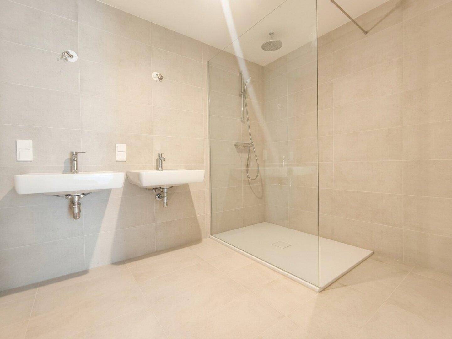 Modernes Badezimmer mit zwei Waschbecken, großer begehbarer Dusche und hellen Fliesen.