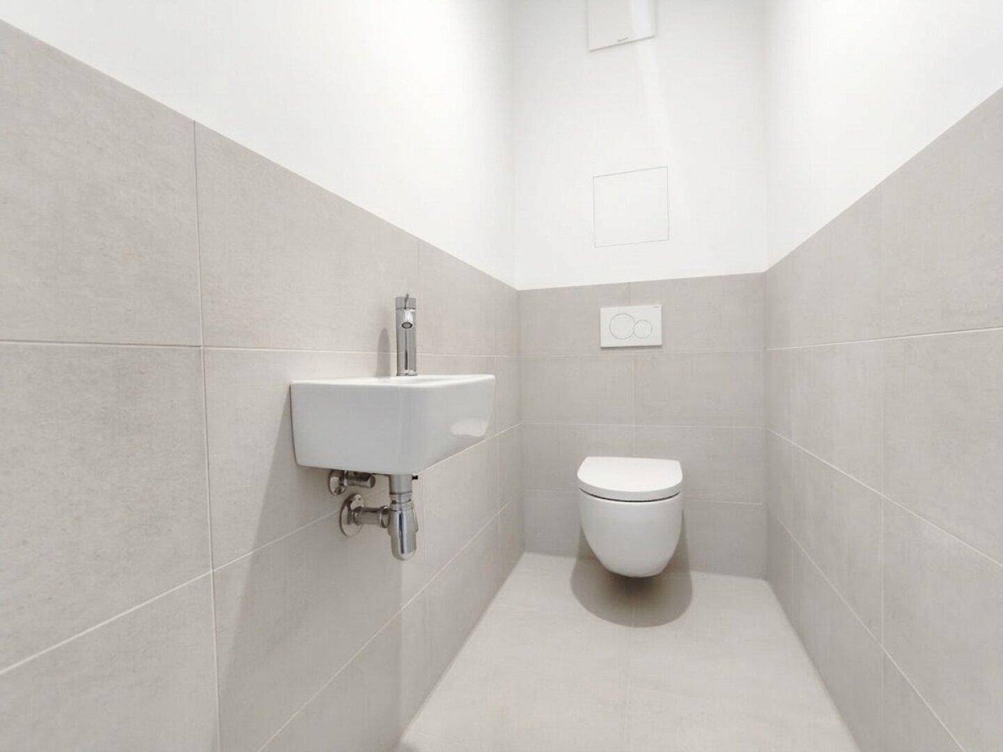 Kleines Gäste-WC mit wandhängender Toilette und modernem Waschbecken in hellen Fliesen.