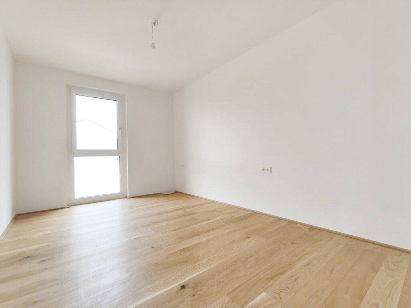 Freundliches Zimmer mit hellem Holzplankenboden und einem großen Fenster für natürliche Belichtung.