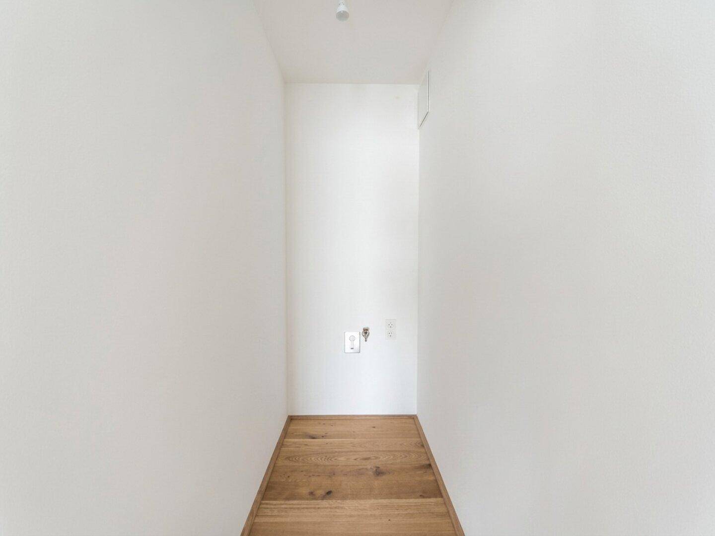 Praktischer Hauswirtschaftsraum mit weißen Wänden und hellem Holzplankenboden für Anschlüsse.
