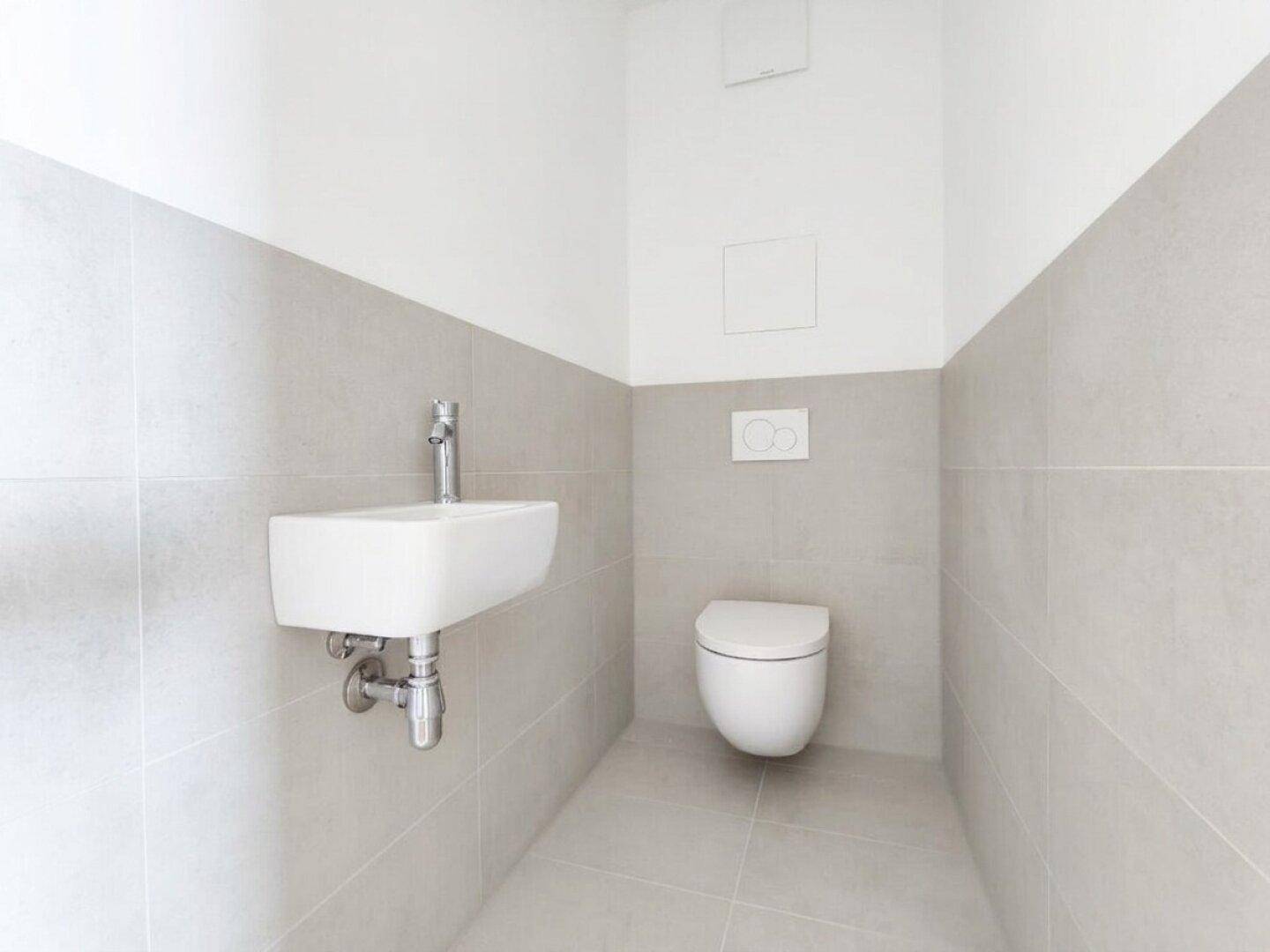 Funktionelles Gäste-WC mit hellgrauen Fliesen, wandhängendem WC und kleinem Waschbecken.