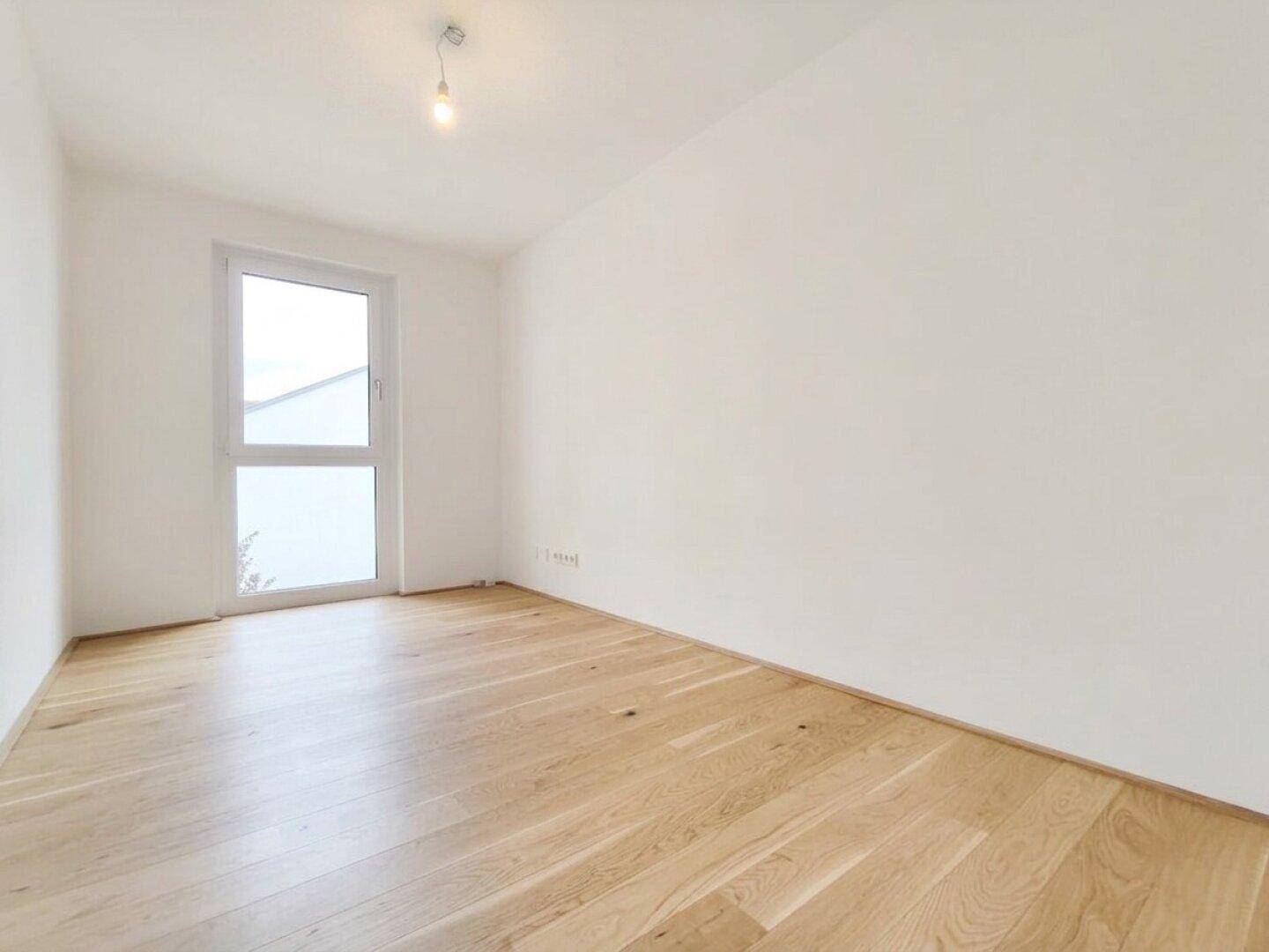 Schlichtes Zimmer mit Holzplankenboden und einem Fenster, das für angenehmes Licht sorgt.