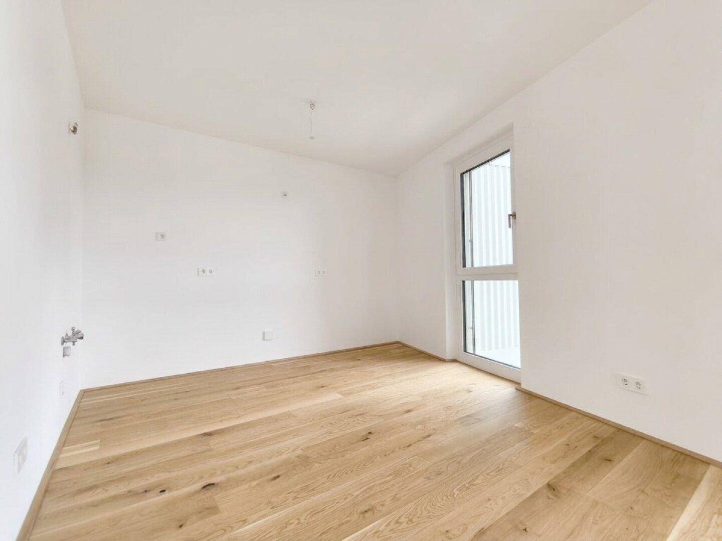 Helles Zimmer mit Holzplankenboden und einem Fenster, das viel Tageslicht hereinlässt.