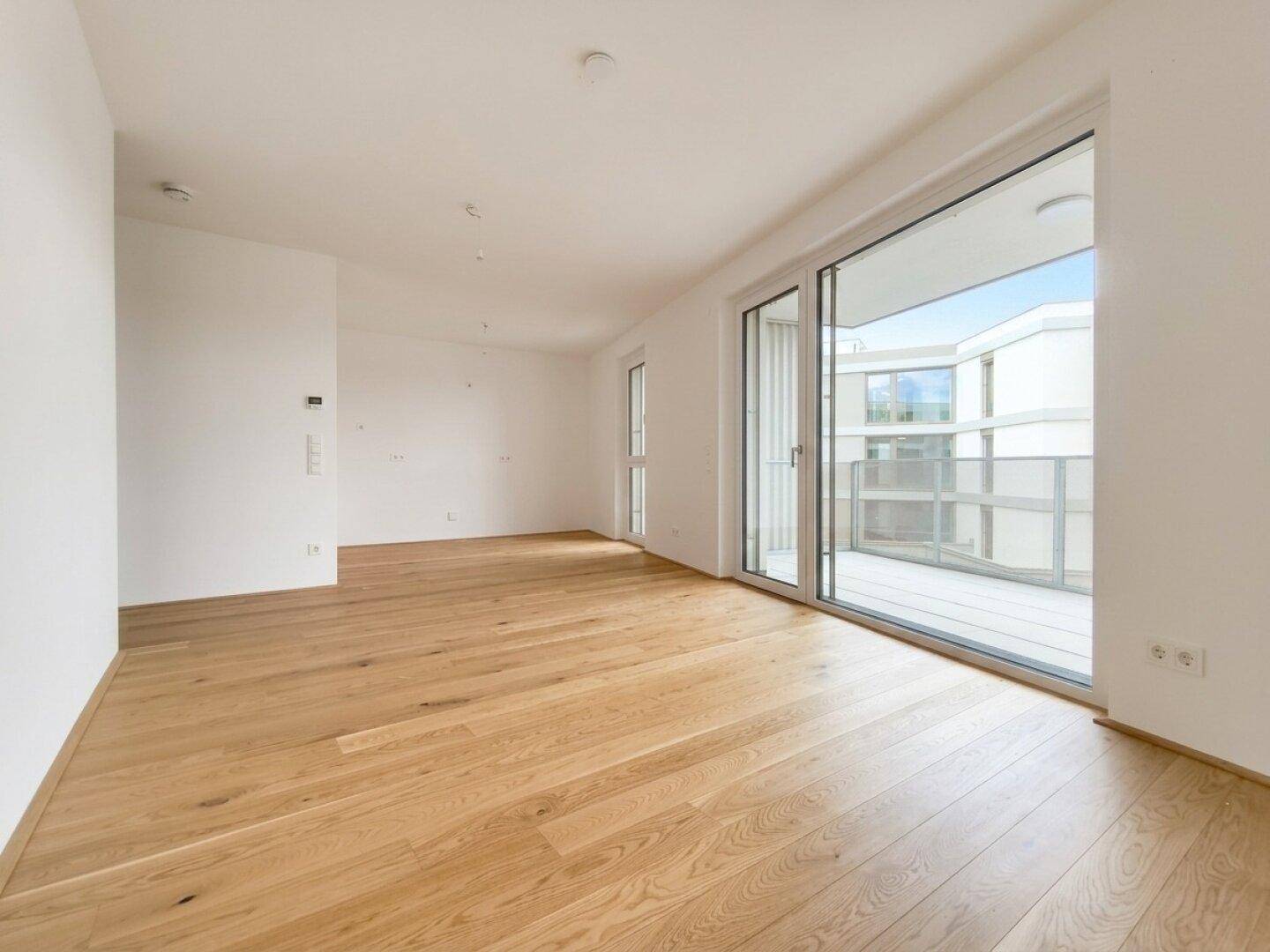 Lichtdurchfluteter Raum mit hellem Holzplankenboden und großem Zugang zu einem Balkon.