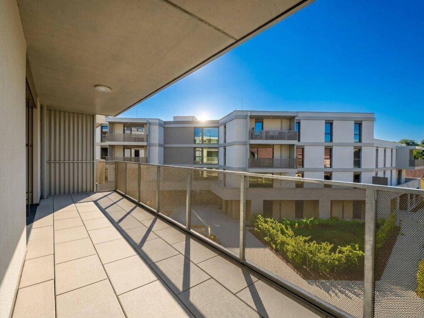 Geräumiger Balkon mit Fliesenboden und Blick auf die moderne Architektur des Gebäudekomplexes.