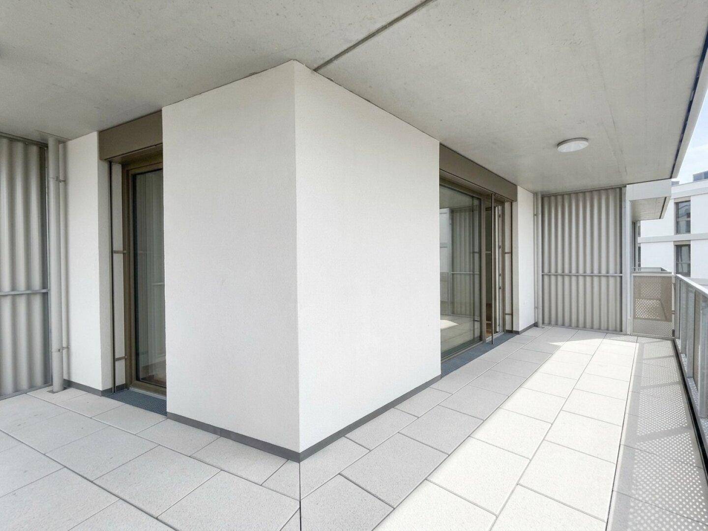 Heller Balkon mit Fliesenboden und großen Schiebetüren, die viel Tageslicht in die Innenräume lassen.