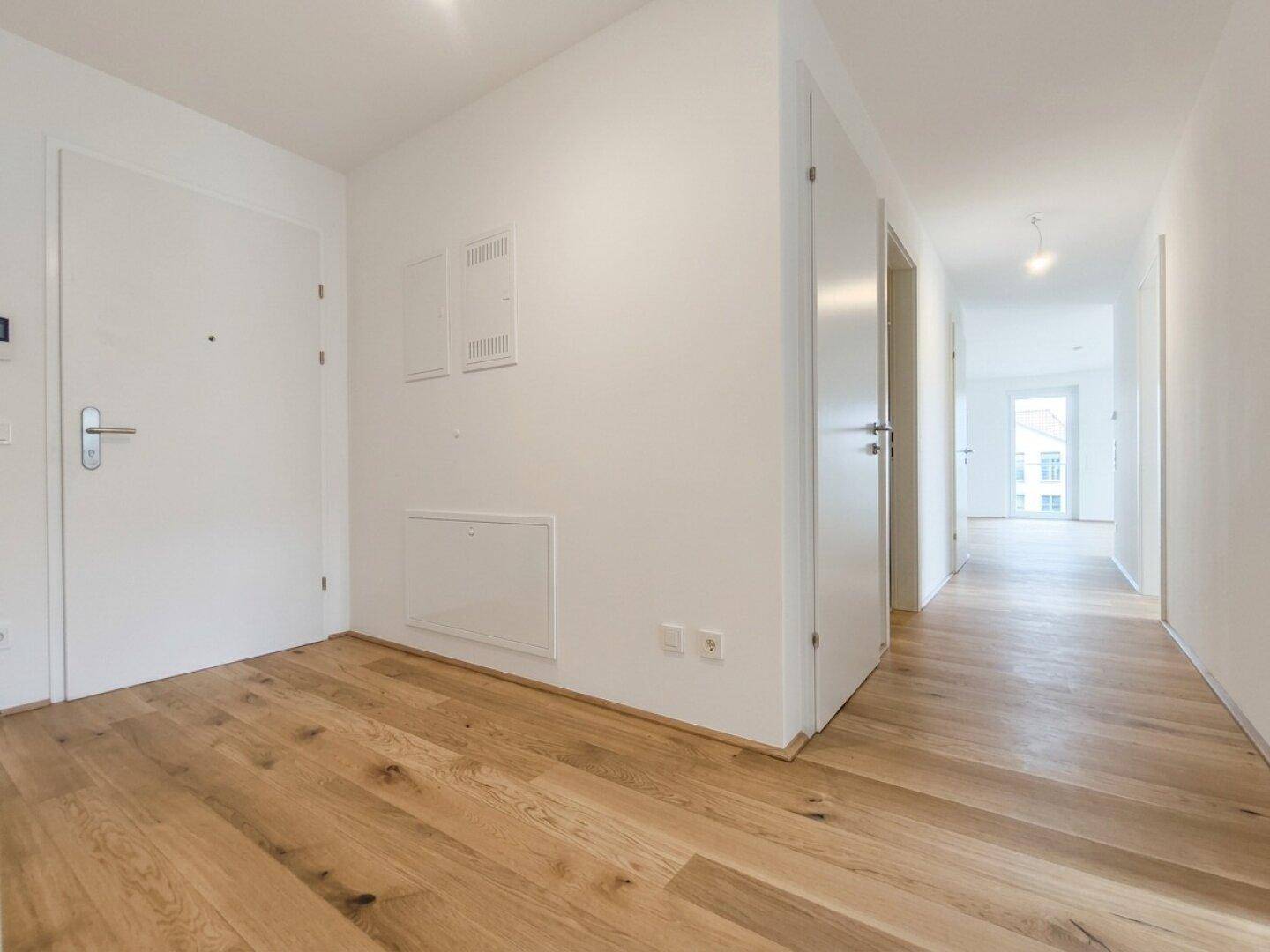 Heller Eingangsbereich und Flur mit Parkettboden und weißen Türen, die zu den Zimmern führen.
