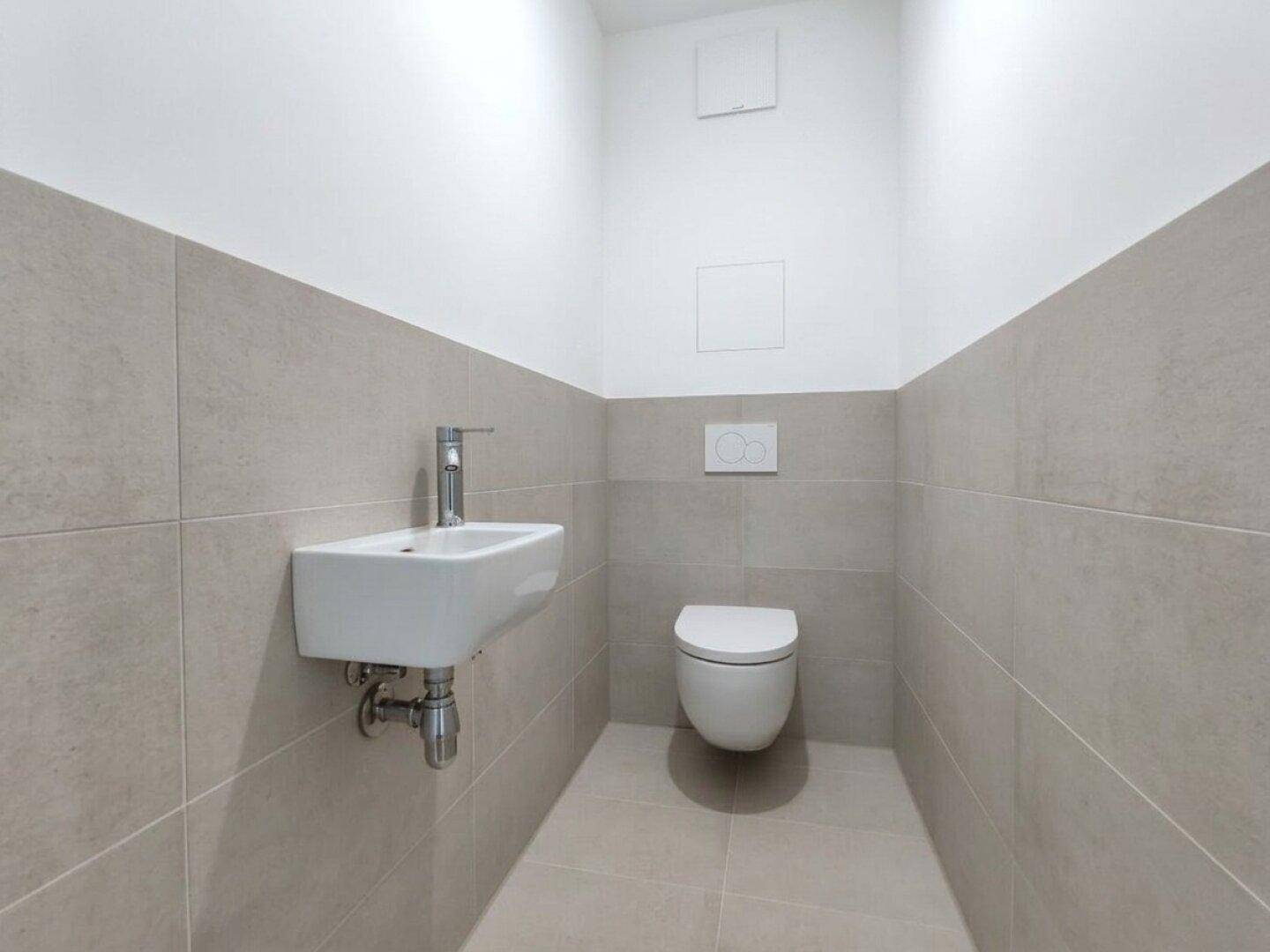 Separates Gäste-WC mit Wand-WC und kleinem Handwaschbecken in modernem Design.