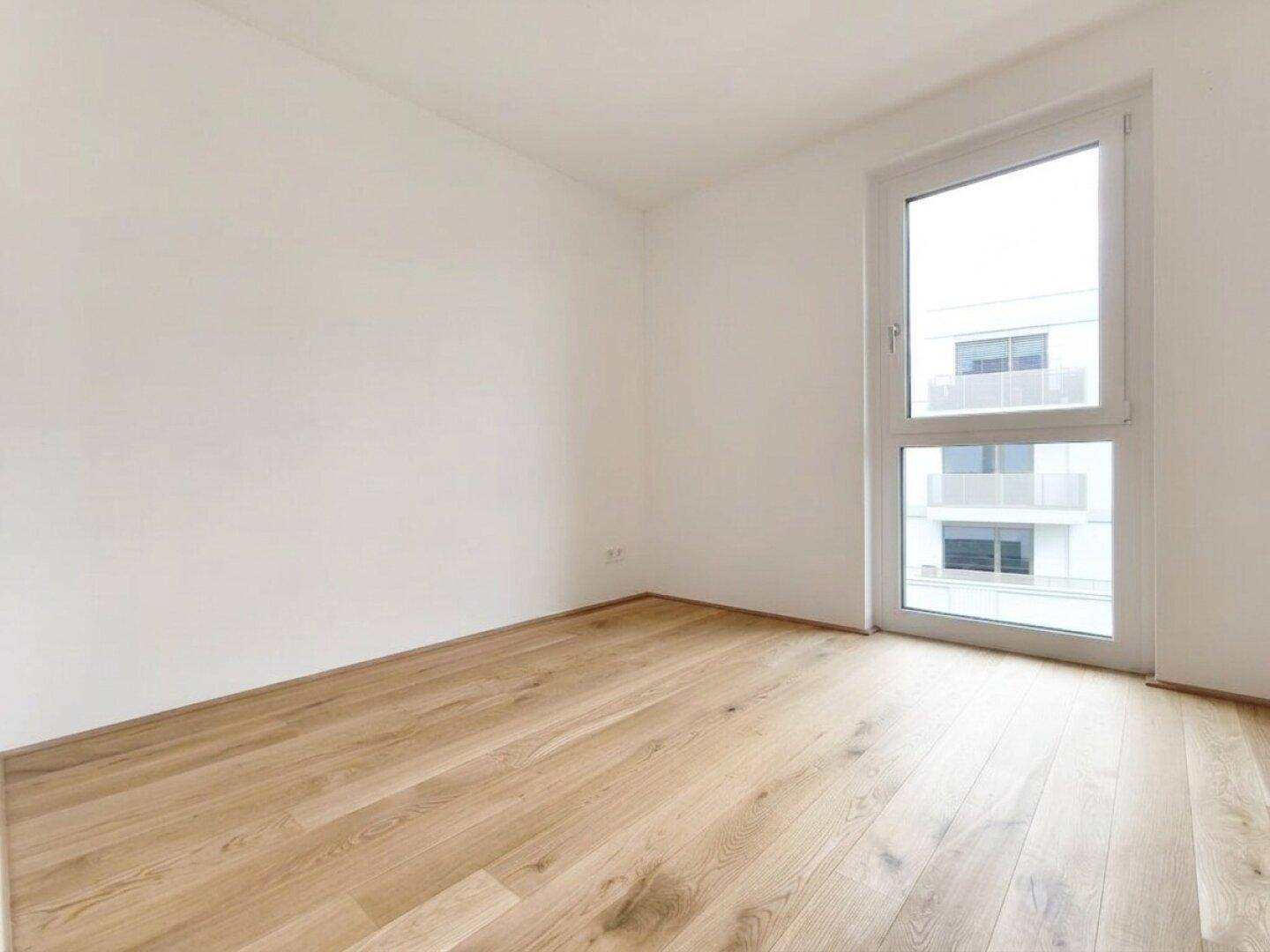 Lichtdurchflutetes Schlafzimmer mit Parkettboden und modernem Fensterrahmen.