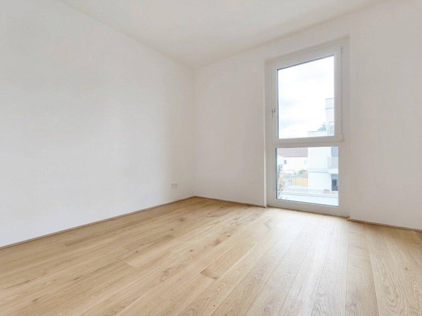 Helles Schlafzimmer mit Parkettboden und großem Fenster, bereit zur individuellen Gestaltung.