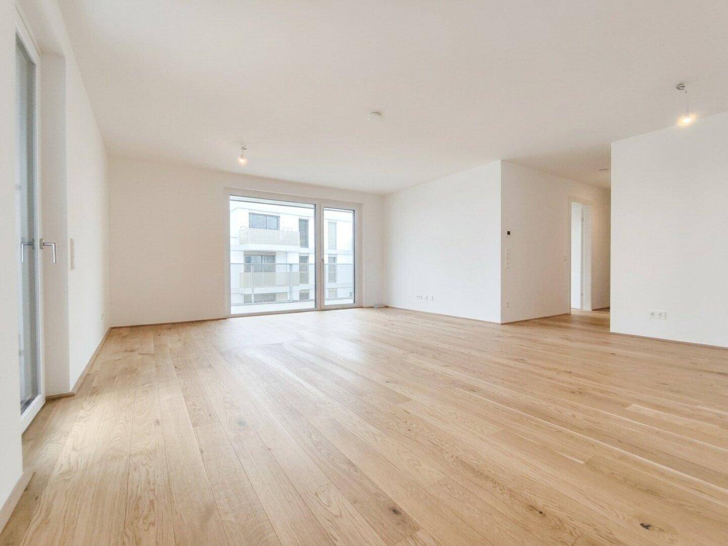 Geräumiges Wohnzimmer mit hellem Parkettboden und Blick auf die umliegenden Gebäude.