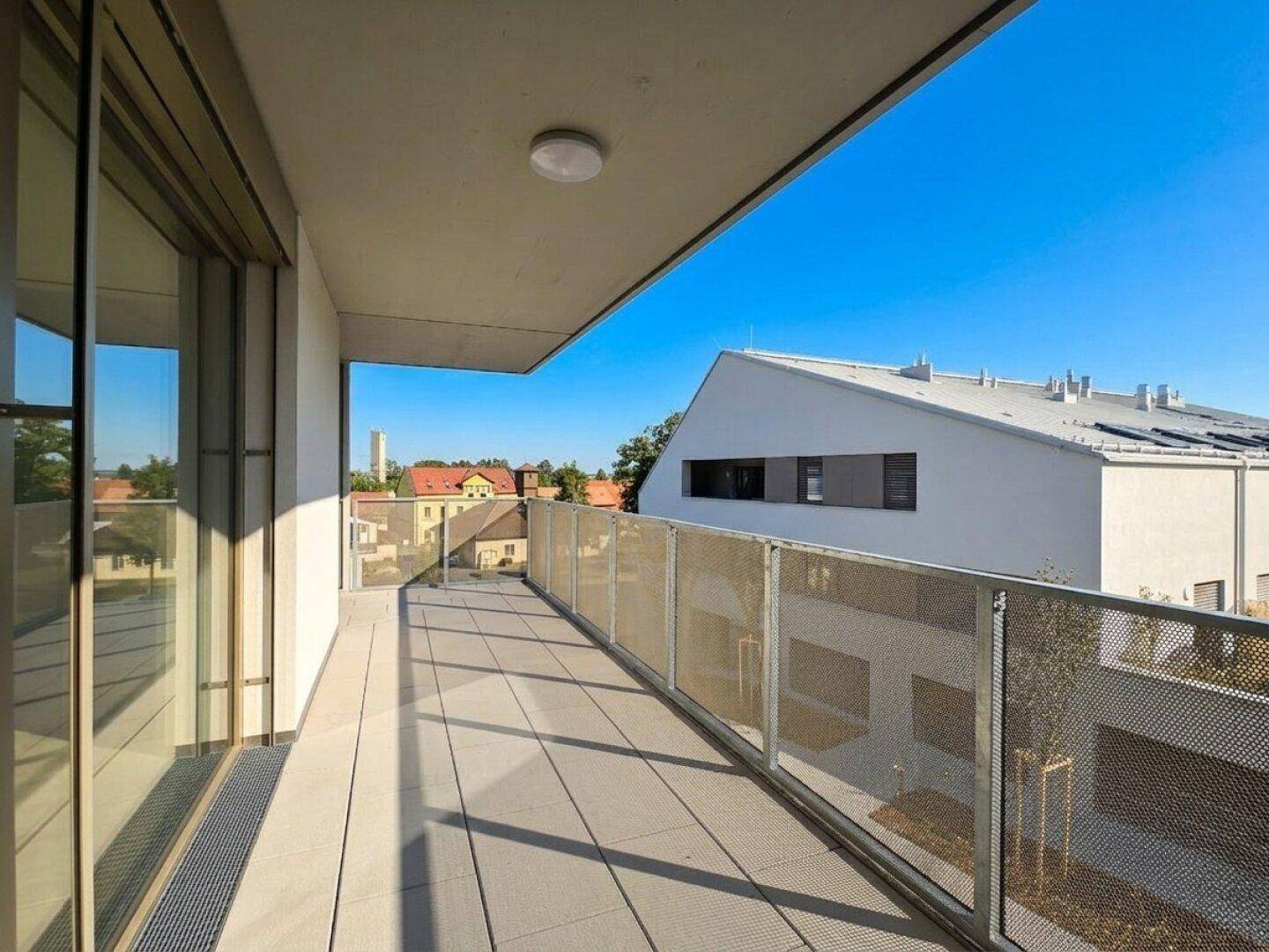 Moderner Balkon mit Fliesenboden und Metallgeländer unter blauem Himmel.