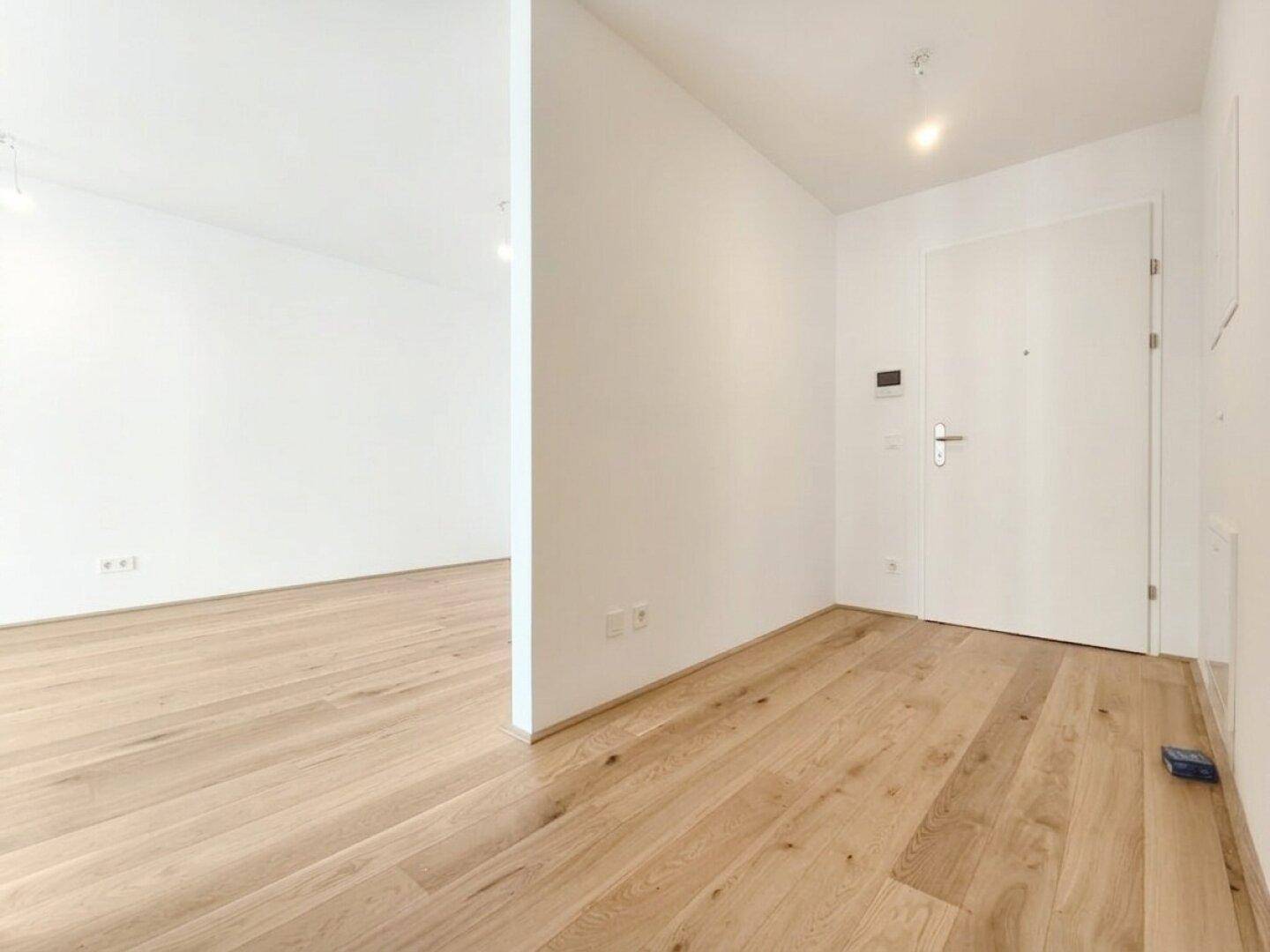 Heller Eingangsbereich mit Holzparkett und weißer Eingangstür, der zu den Wohnräumen führt.