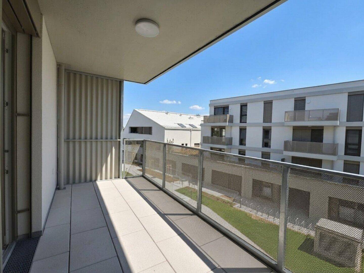 Geräumiger Balkon mit Fliesenboden und Blick auf den Innenhof und moderne Gebäude.