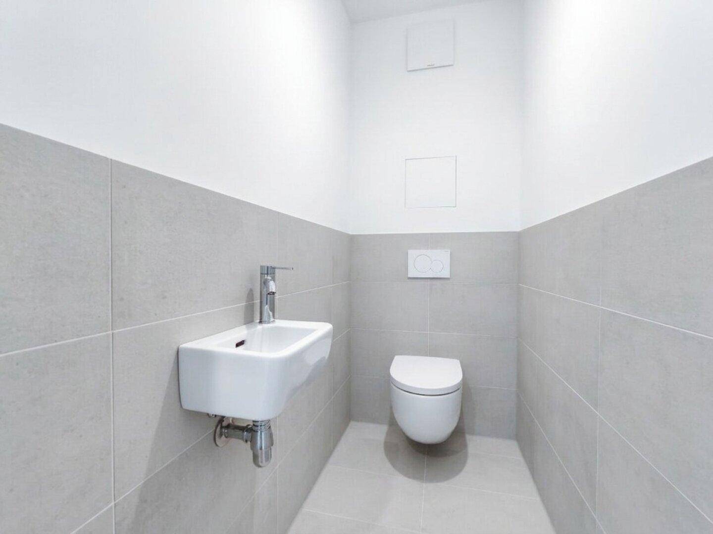 Separates Gäste-WC mit modernen grauen Fliesen, wandhängender Toilette und kleinem Waschbecken.