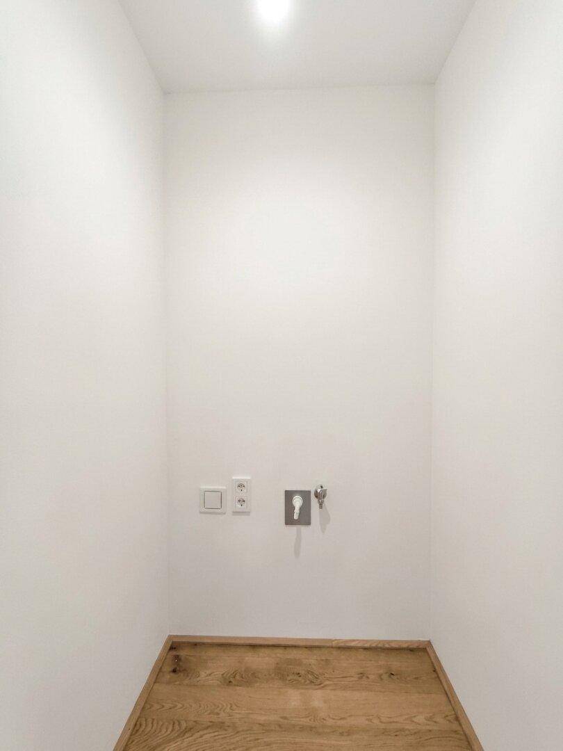 Praktischer Hauswirtschaftsraum mit Anschlüssen und hellem Holzparkett, ideal für Waschmaschine und Trockner.
