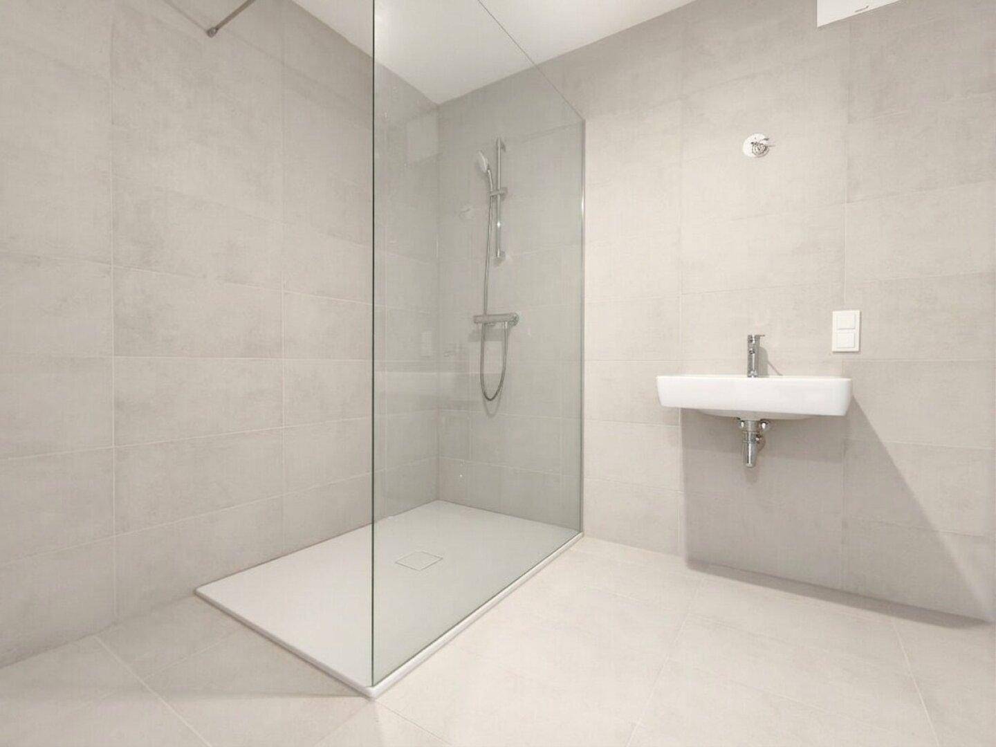 Modernes Badezimmer mit grauen Fliesen, ebenerdiger Dusche und Wandwaschbecken.